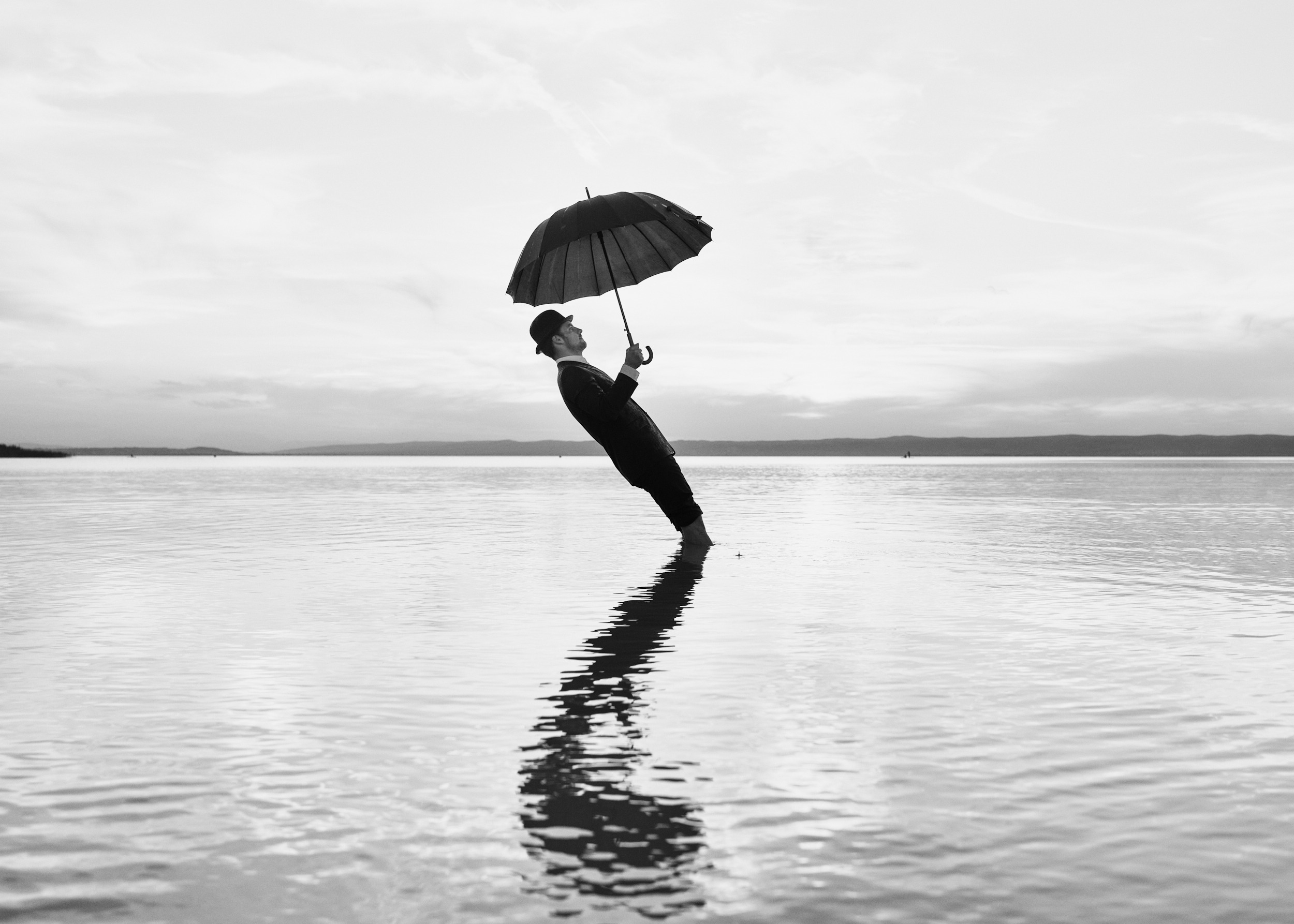 A man with an umbrella leaning back in water above his reflection.