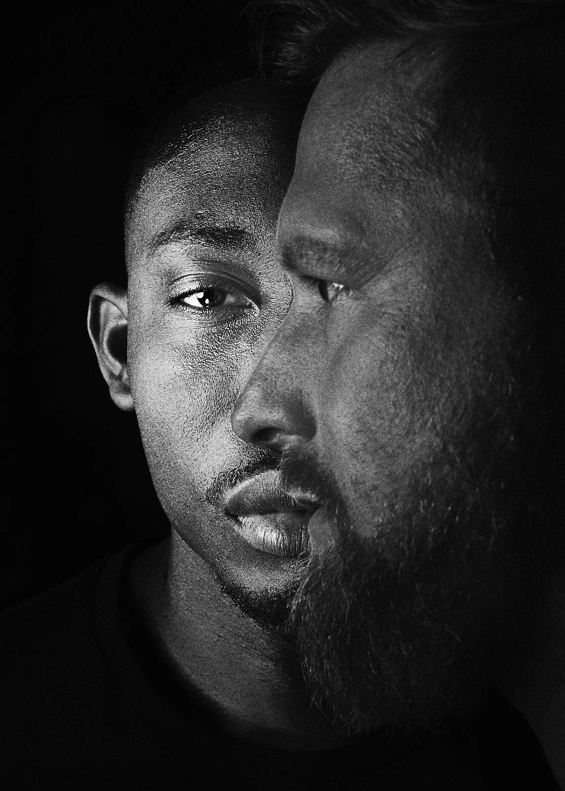 Black and white close-up photo of two people's faces, one of African descent and the other of Asian descent, with their faces very close together, creating an artistic, intimate composition.