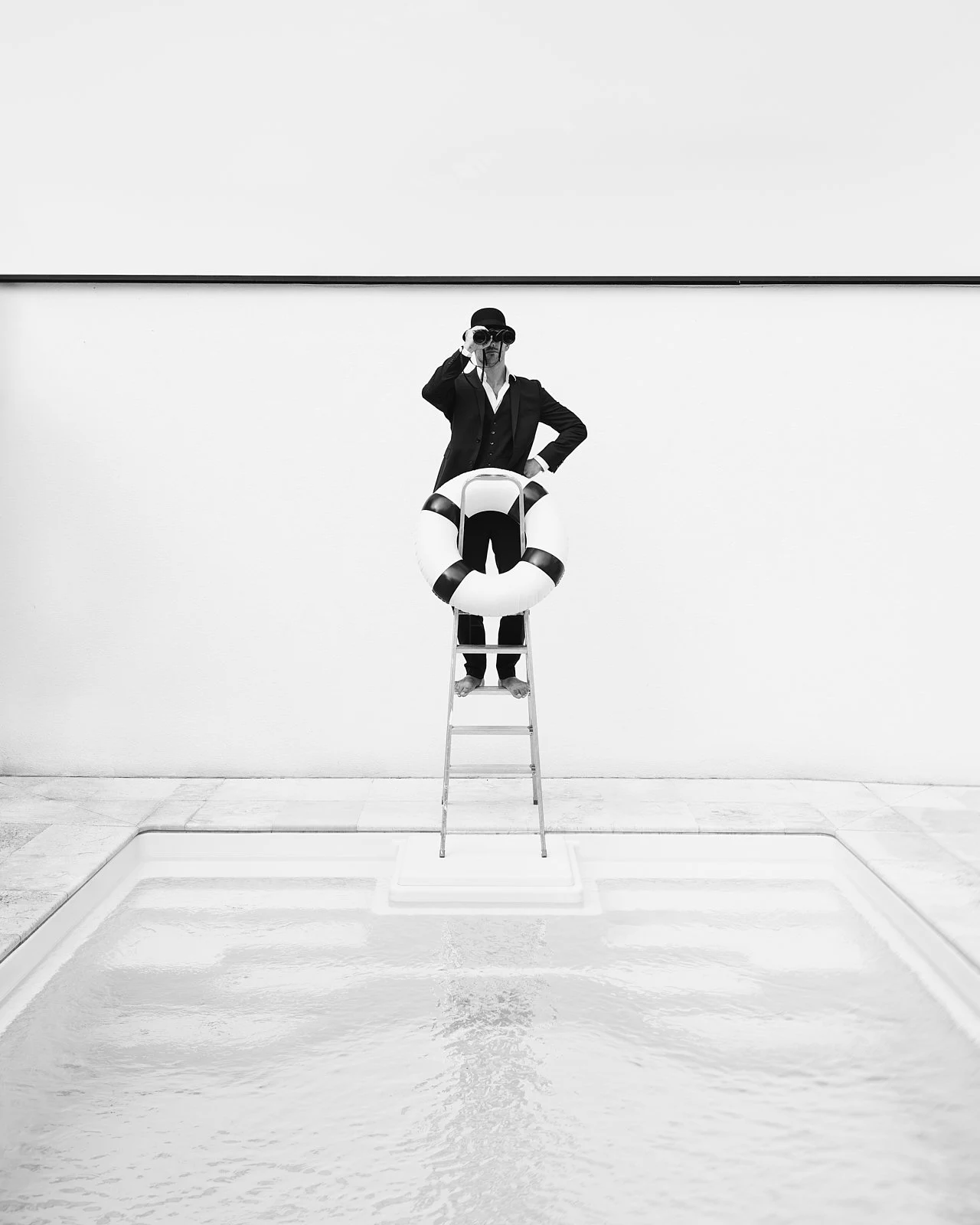 Person dressed in a suit with a lifebuoy around their waist, standing on a ladder next to a swimming pool, taking a photo, in a minimalistic setting, black and white photo.