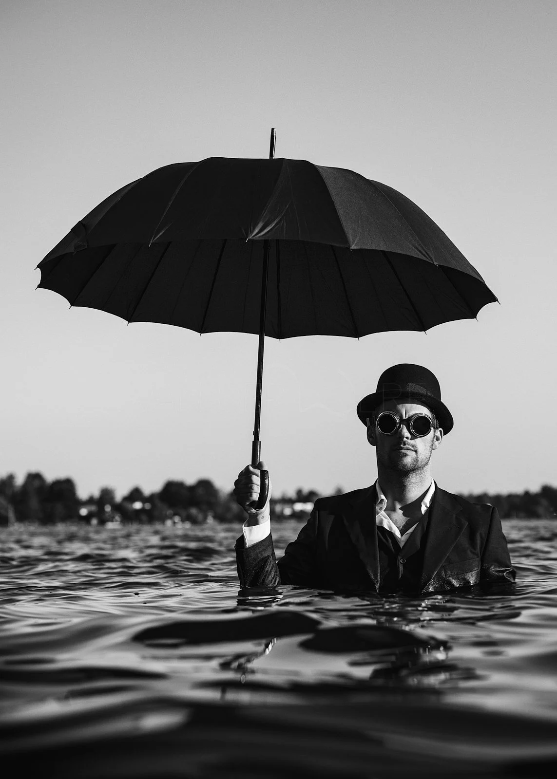 A man in a suit and hat holding an umbrella while standing in water, wearing sunglasses, in black and white