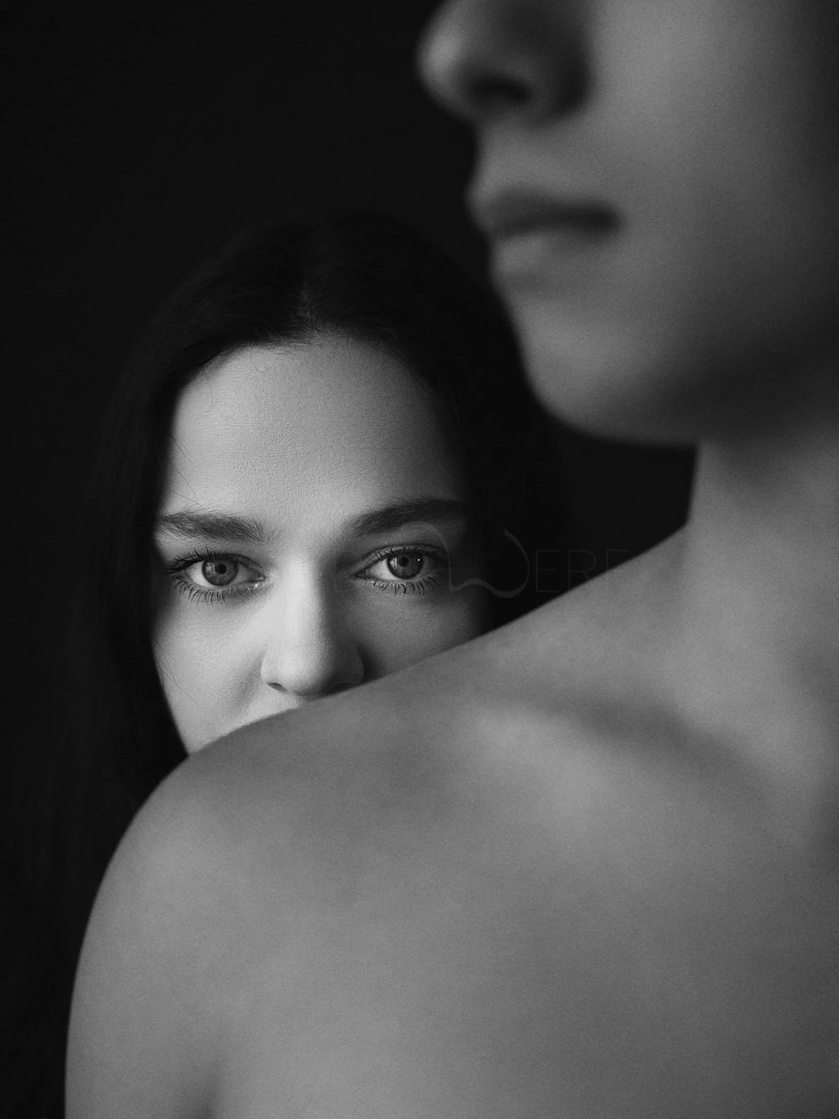 A woman's gaze emerging from behind another person's shoulder.