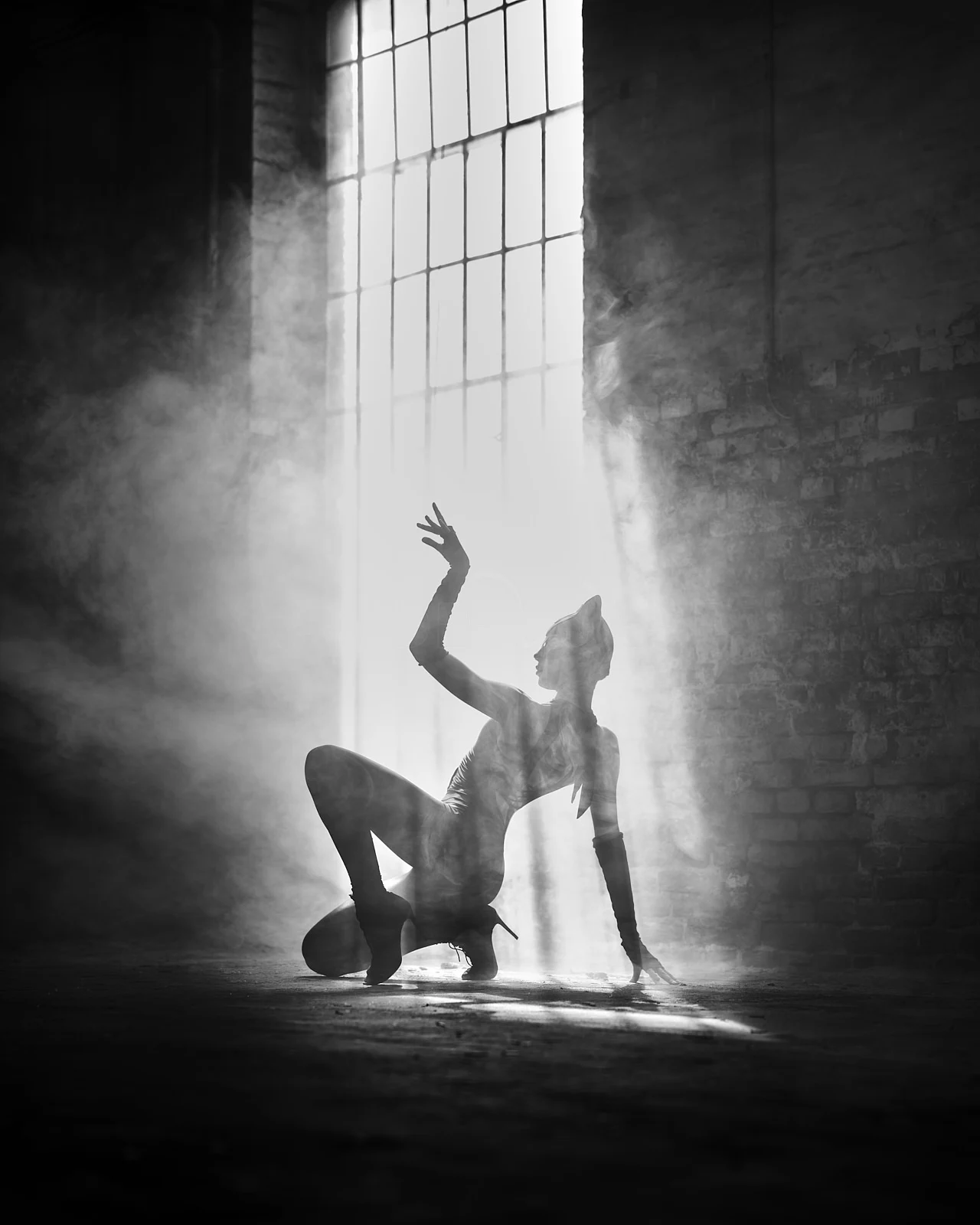 A person bending backwards in a beam of light from a tall studio window.