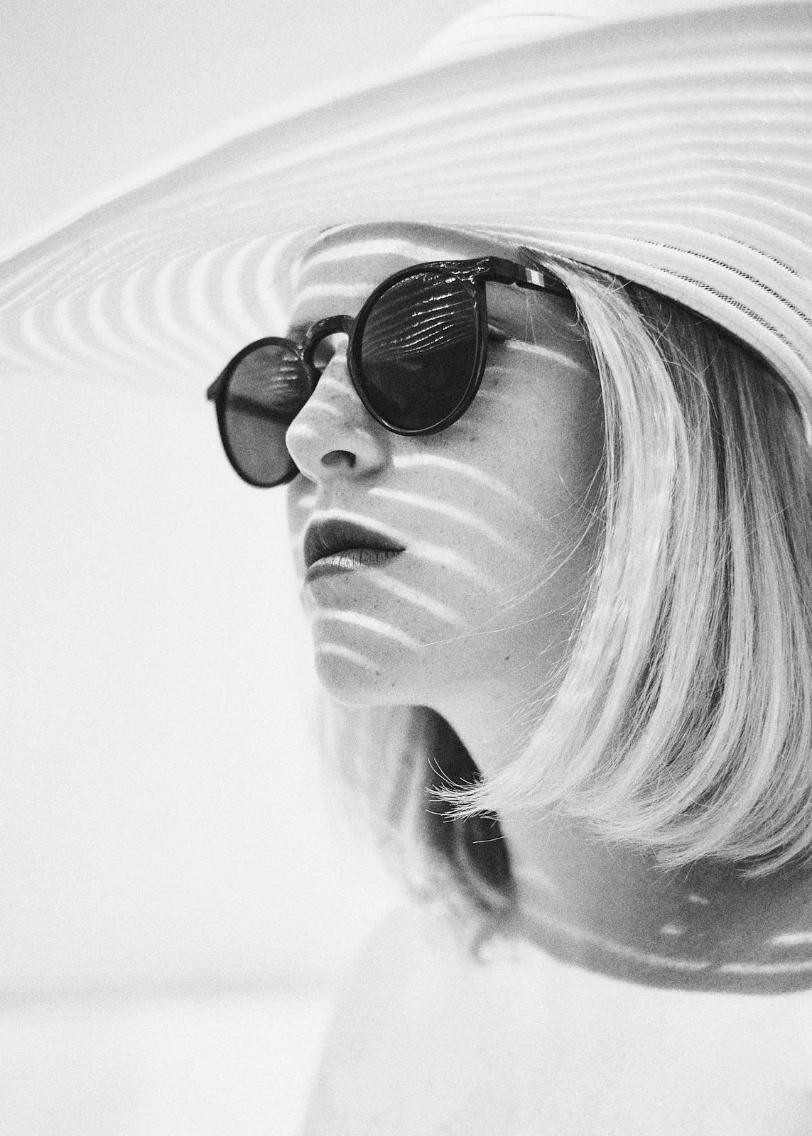 A woman in sunglasses and a pale hat, photographed in bright light.