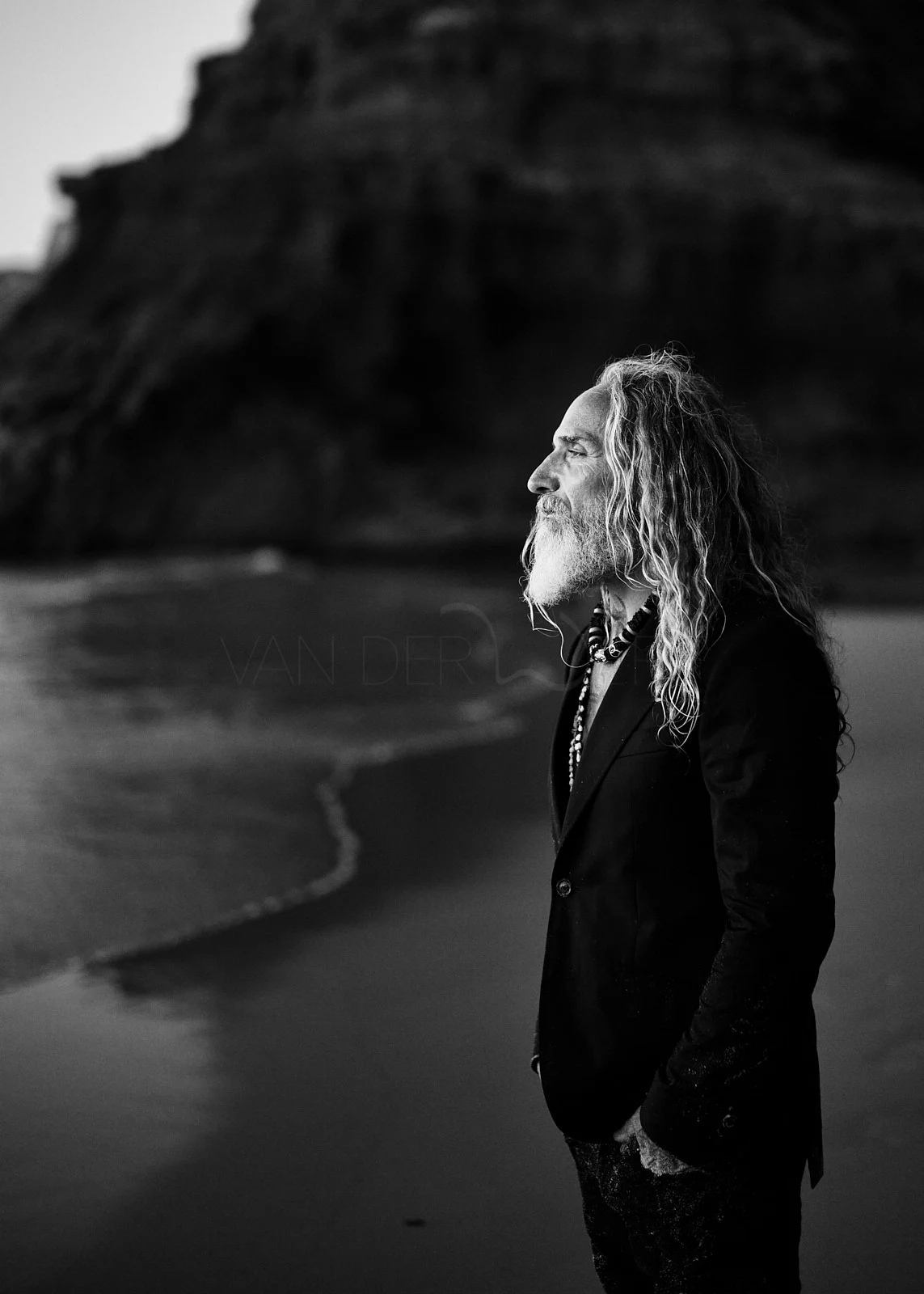 A person standing on a beach beneath a dark rocky cliff.