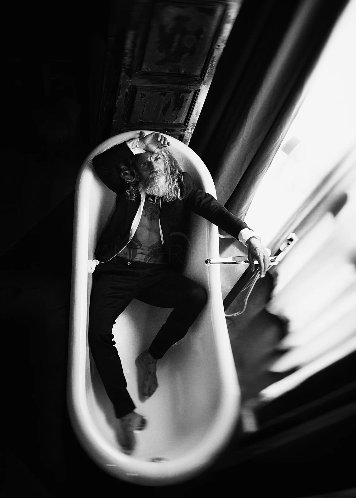 A figure reflected in an oval mirror beside a window.