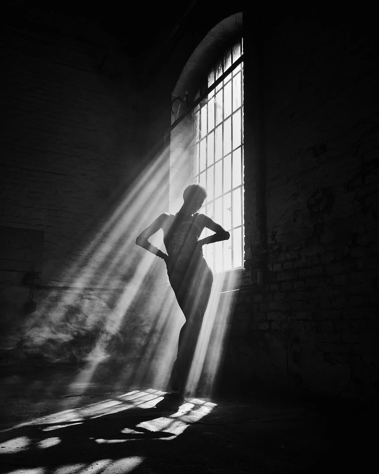 A standing silhouette in diagonal beams of window light.