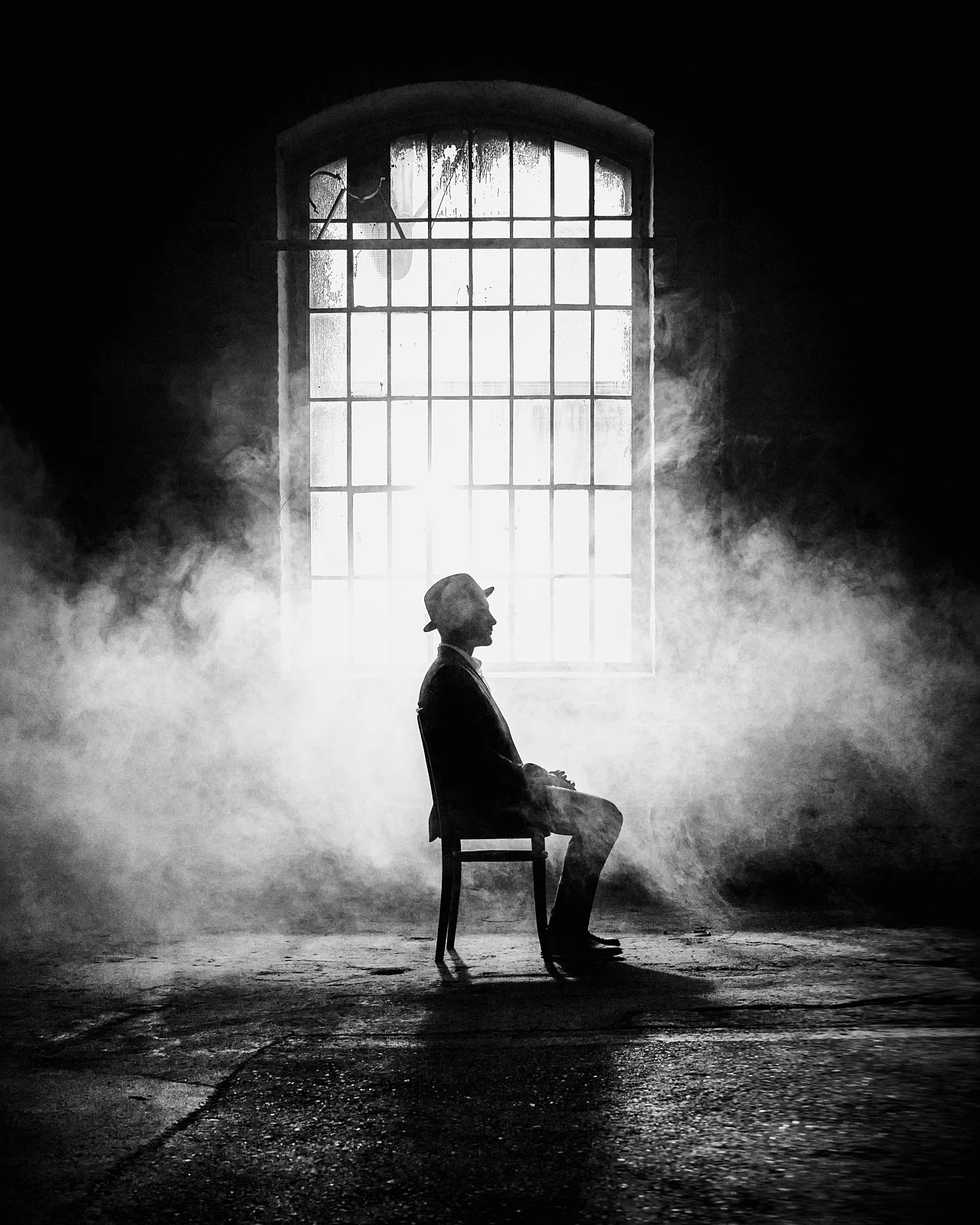 A person seated in profile beneath a luminous studio window.