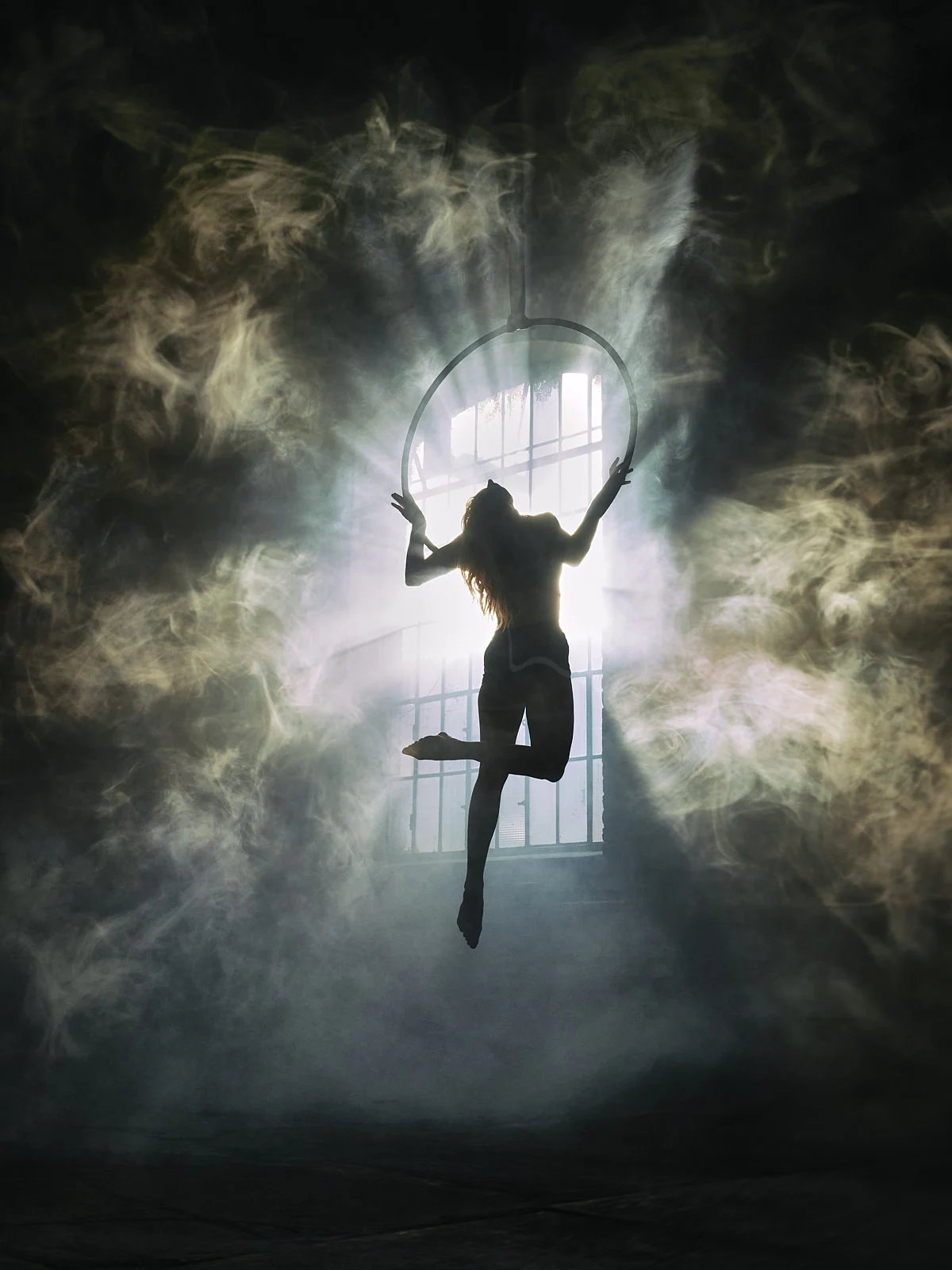 A figure reaching upwards beside a chair in atmospheric window light.