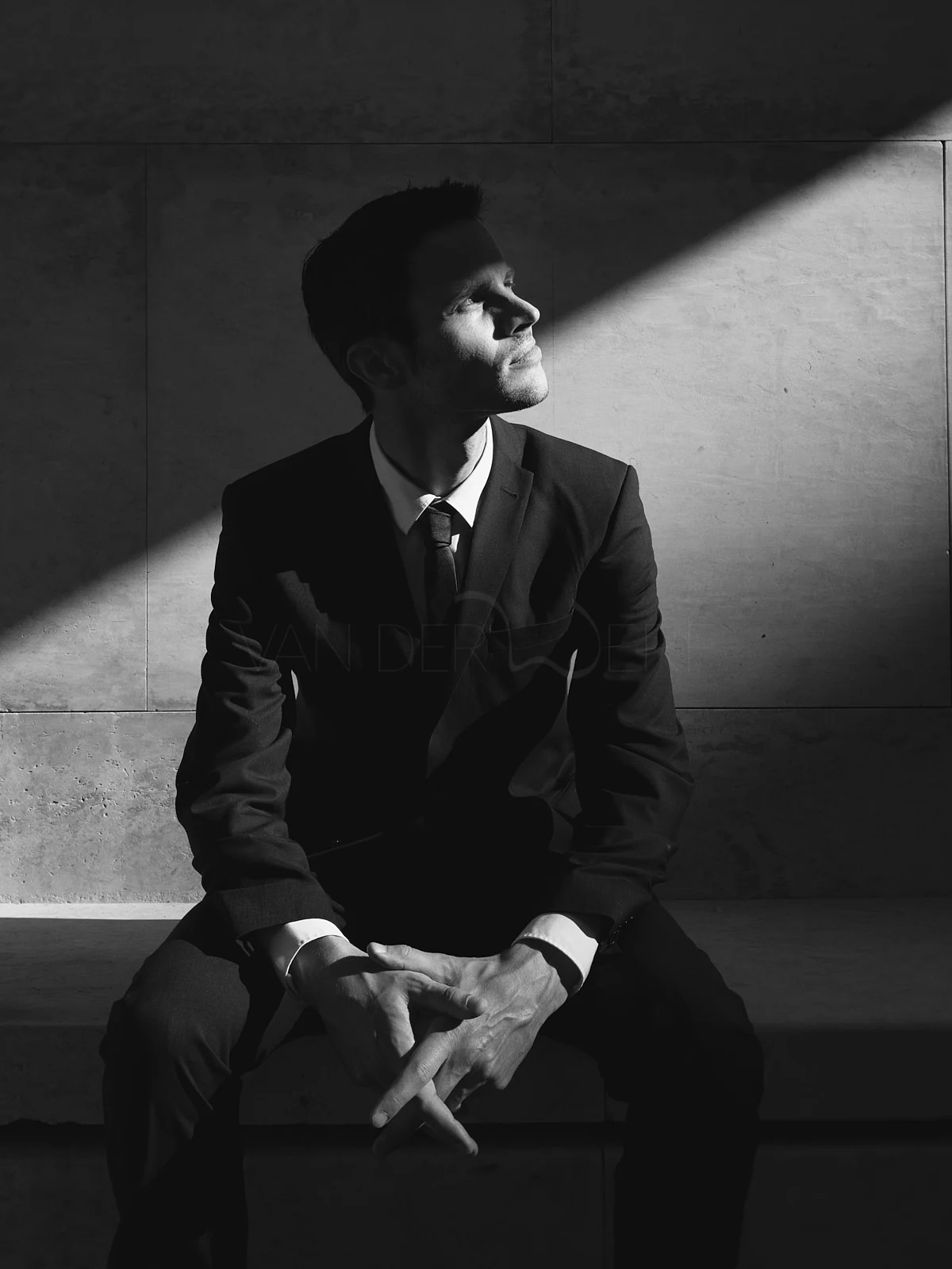 A seated man in a hat looking towards a diagonal beam of light.