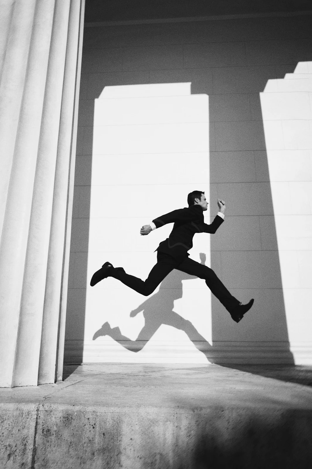 A man running between columns, his shadow following him.
