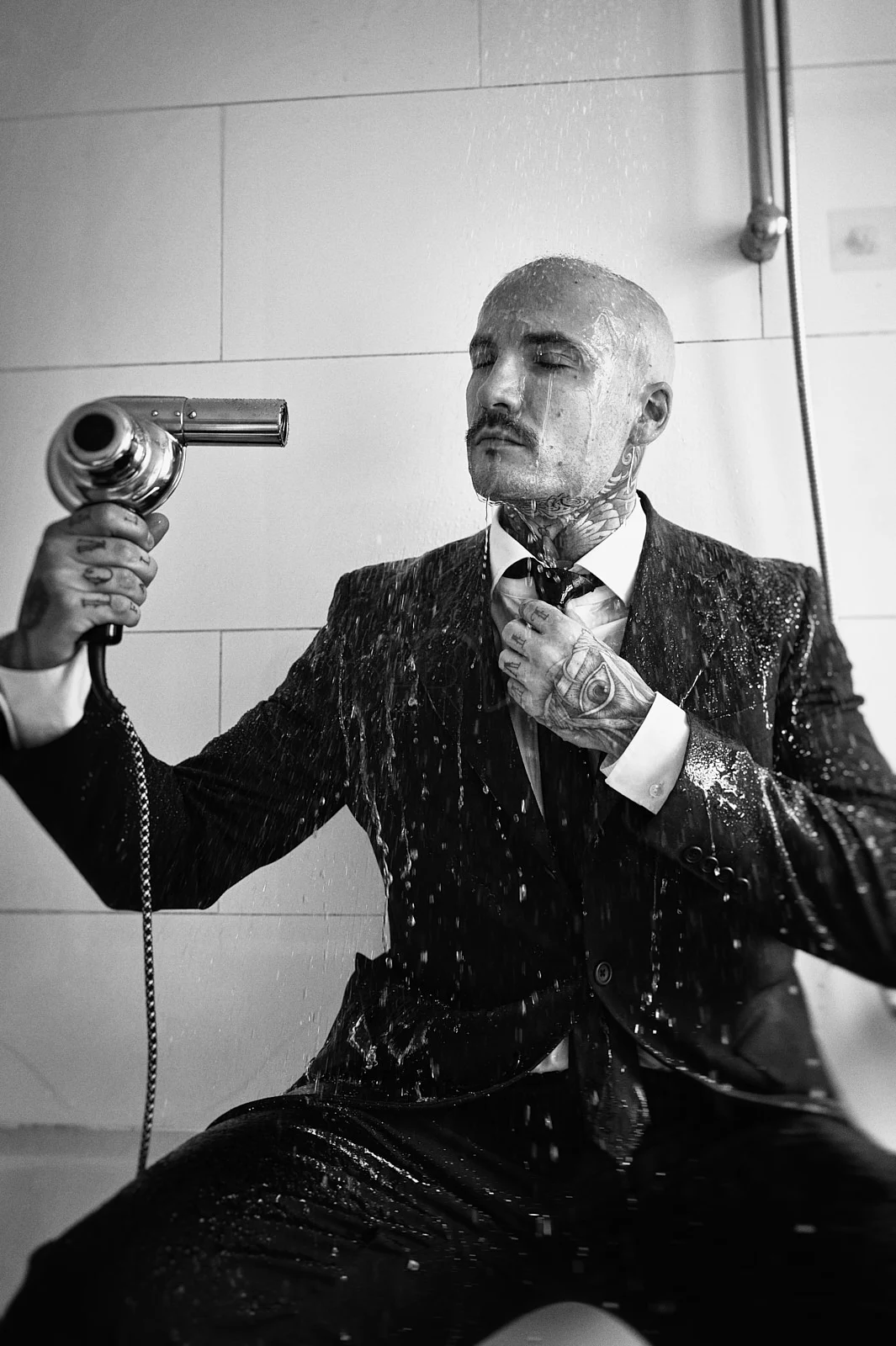 A man in a suit holding a hairdryer as water falls around him.