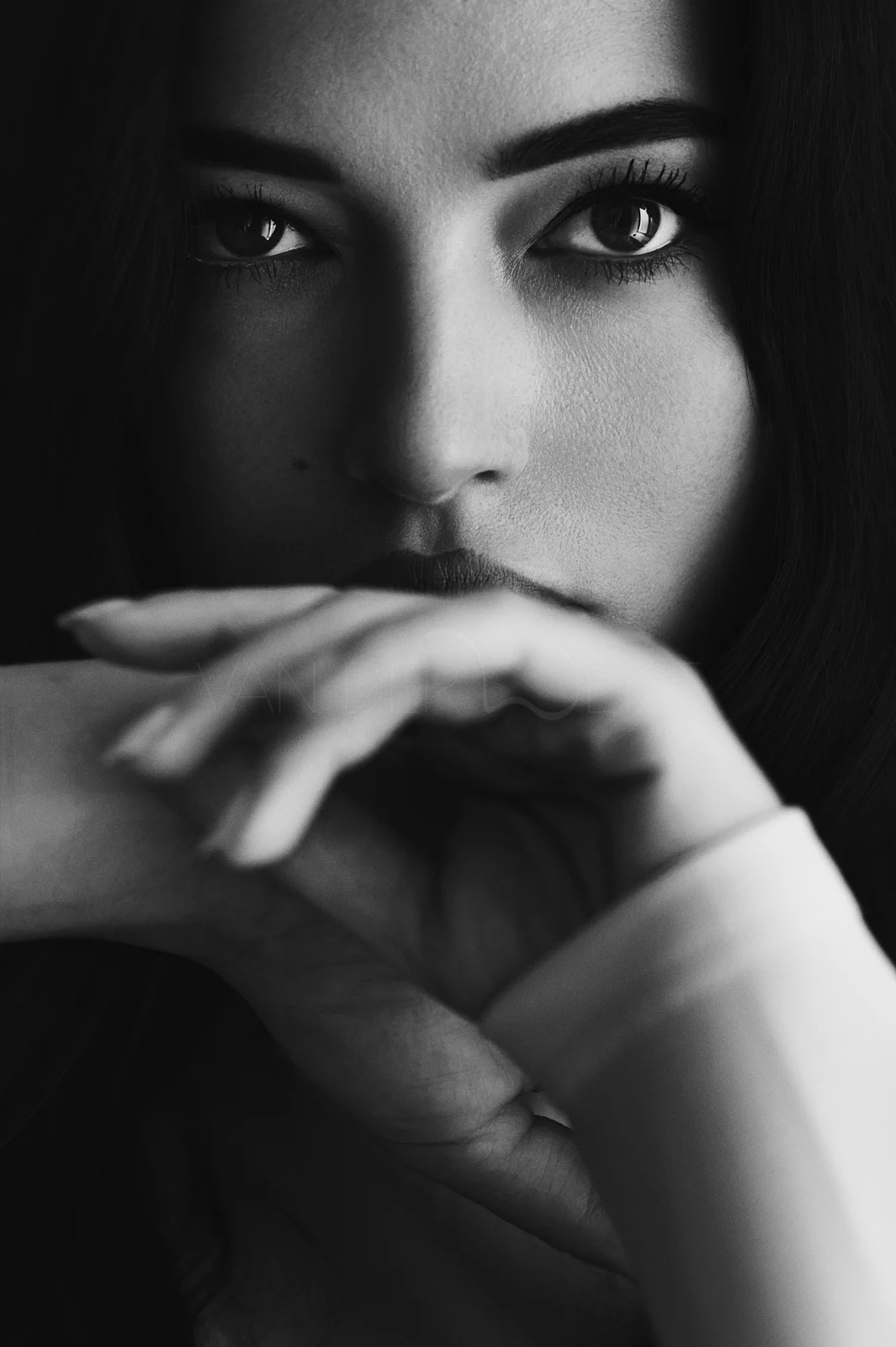 A woman resting her face above folded hands, looking directly into the lens.