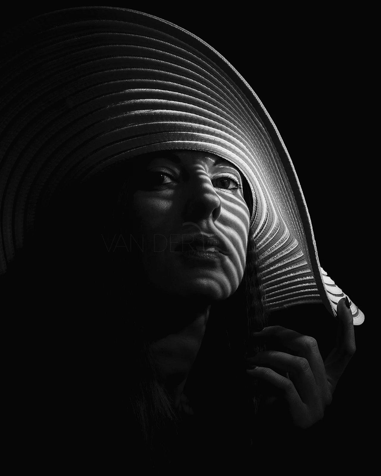 A woman looking upwards beneath a large hat with striped light and shadow.