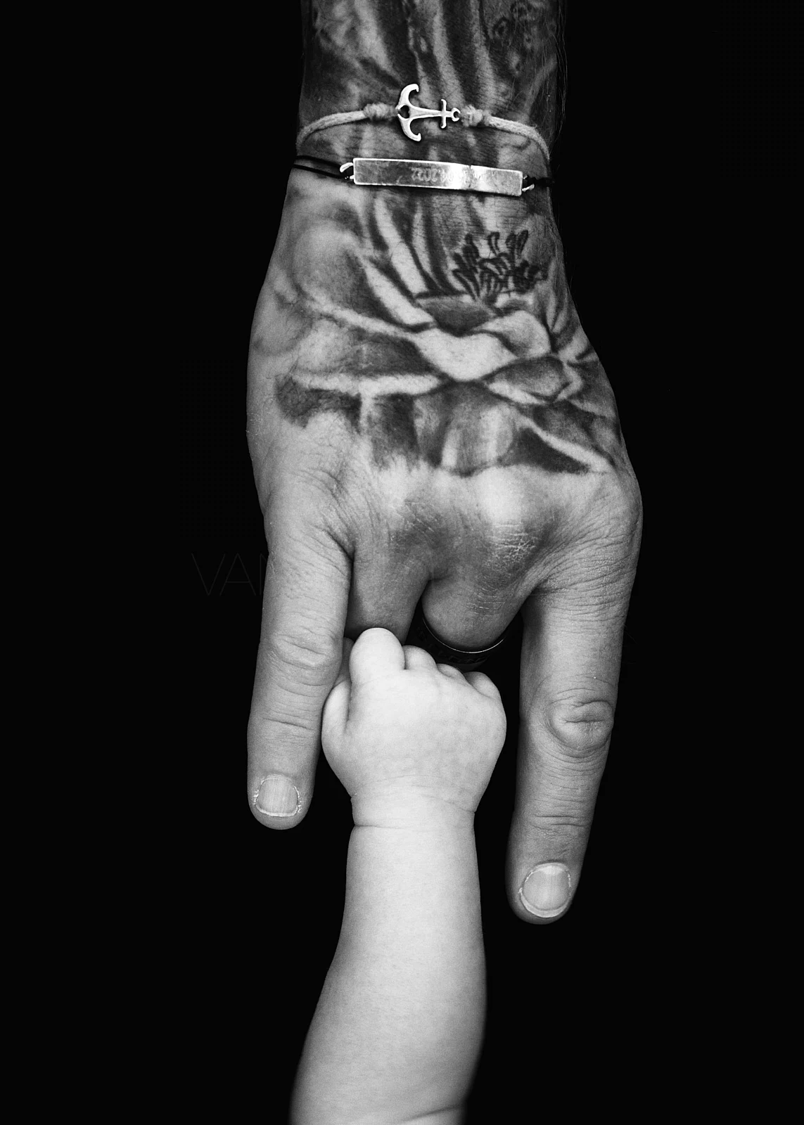 A tattooed adult hand gently holding a small child's hand.