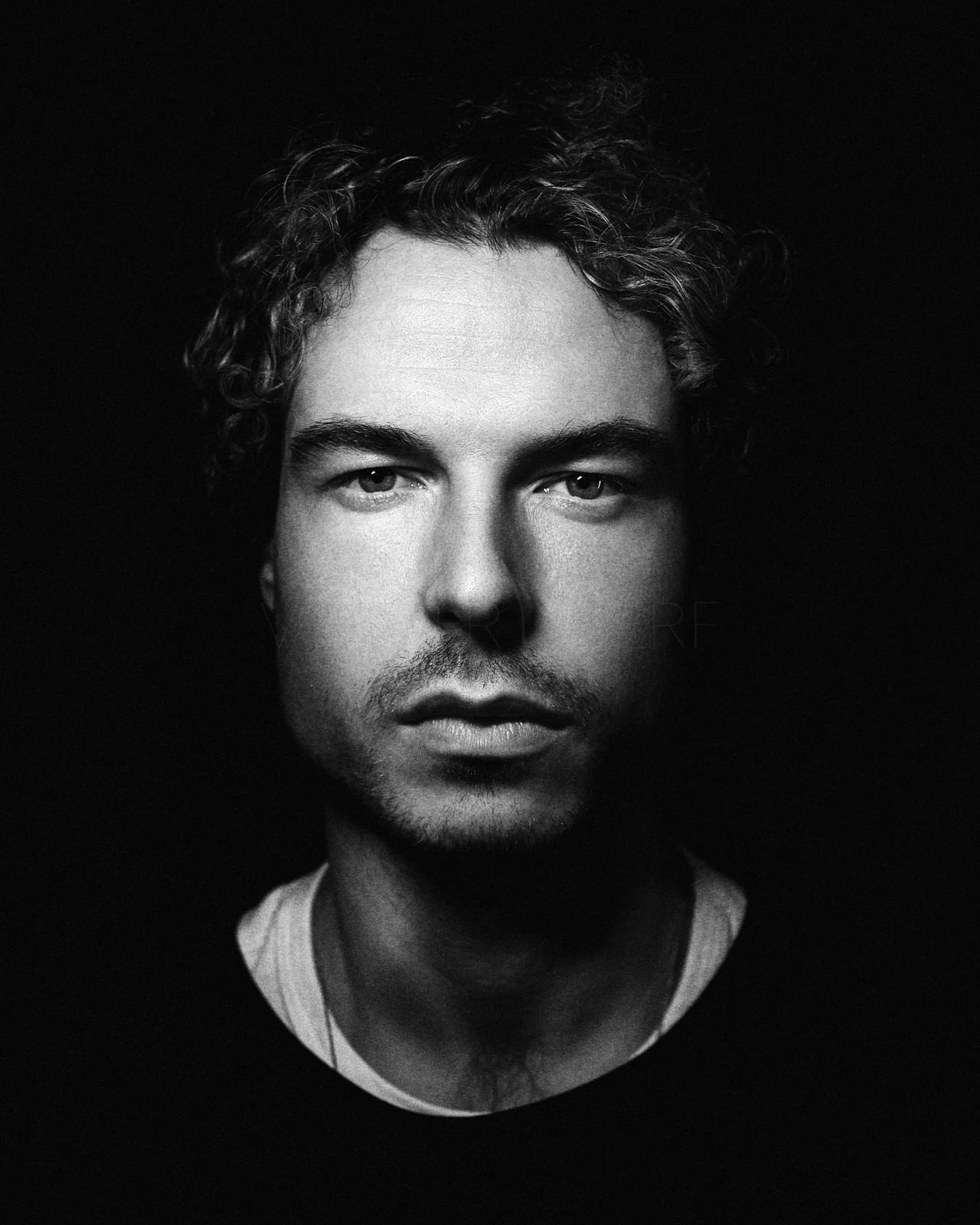 A man with curly hair looking into the camera against a dark background.