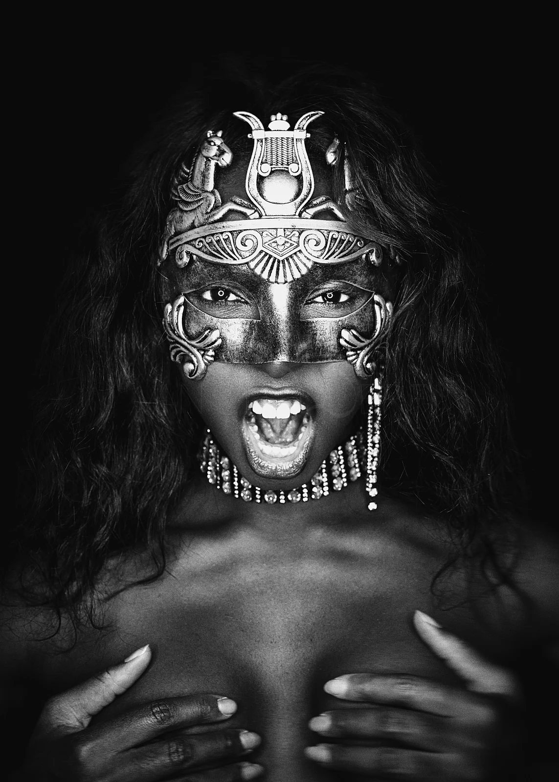 An expressive portrait with an ornate mask, jewellery and hands held against the chest.