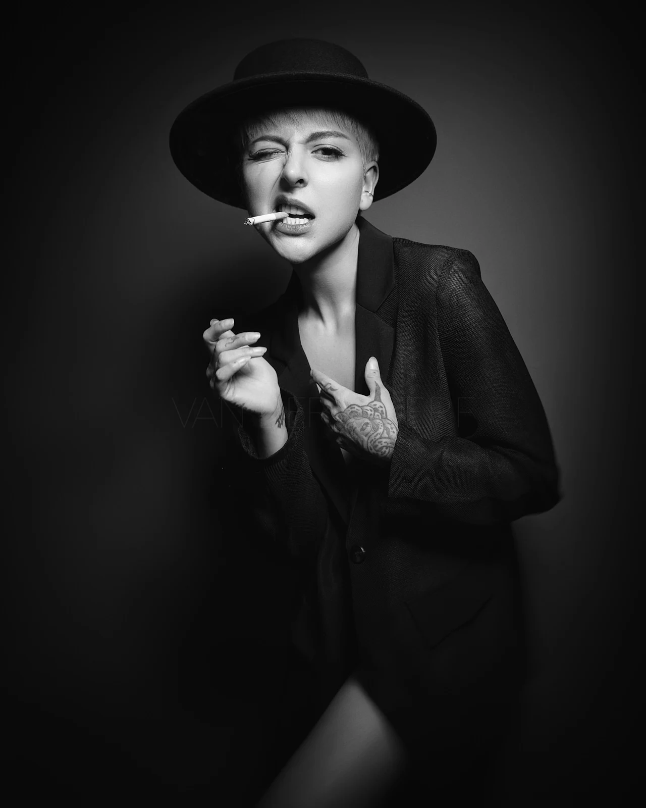 A woman in a hat and blazer winking while holding a cigarette between her lips.