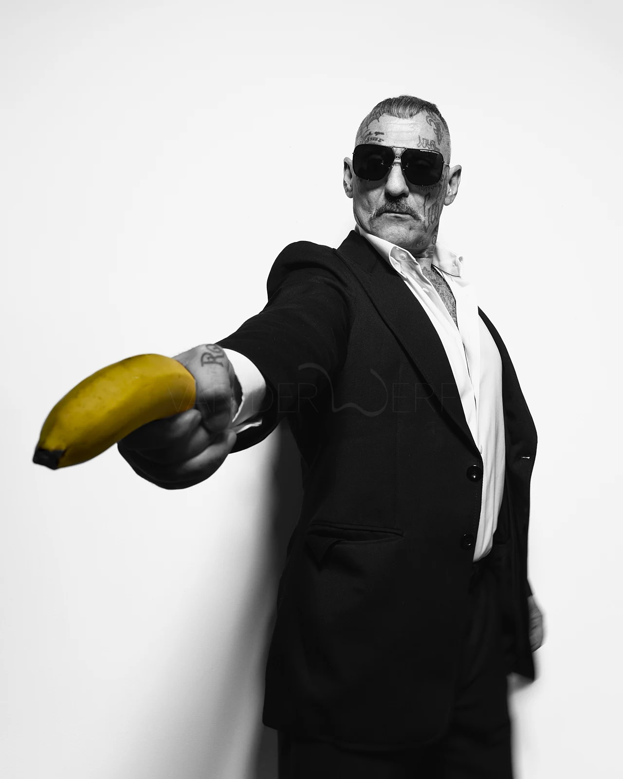 A man in a dark suit presenting a yellow banana towards the camera.