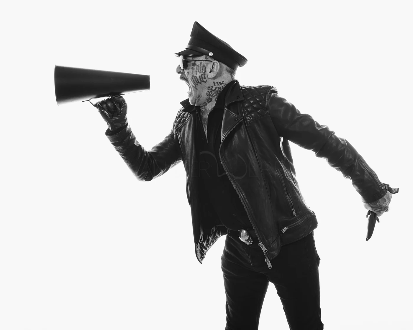 A man in a cap and leather jacket shouting into a megaphone.