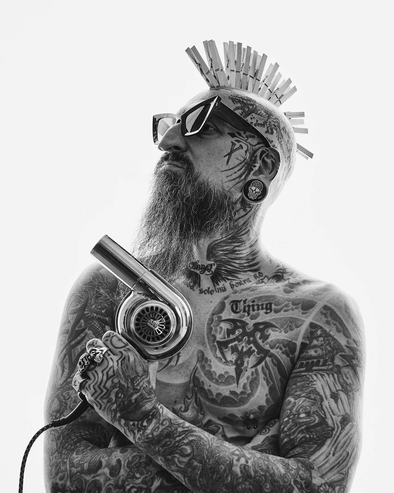 A tattooed man with a beard, sunglasses and clothespins in his hair.
