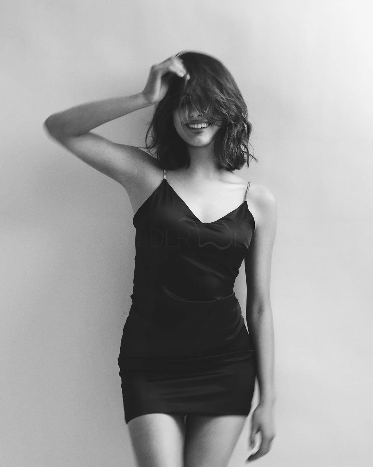 A smiling woman in a dark dress with one hand in her hair.