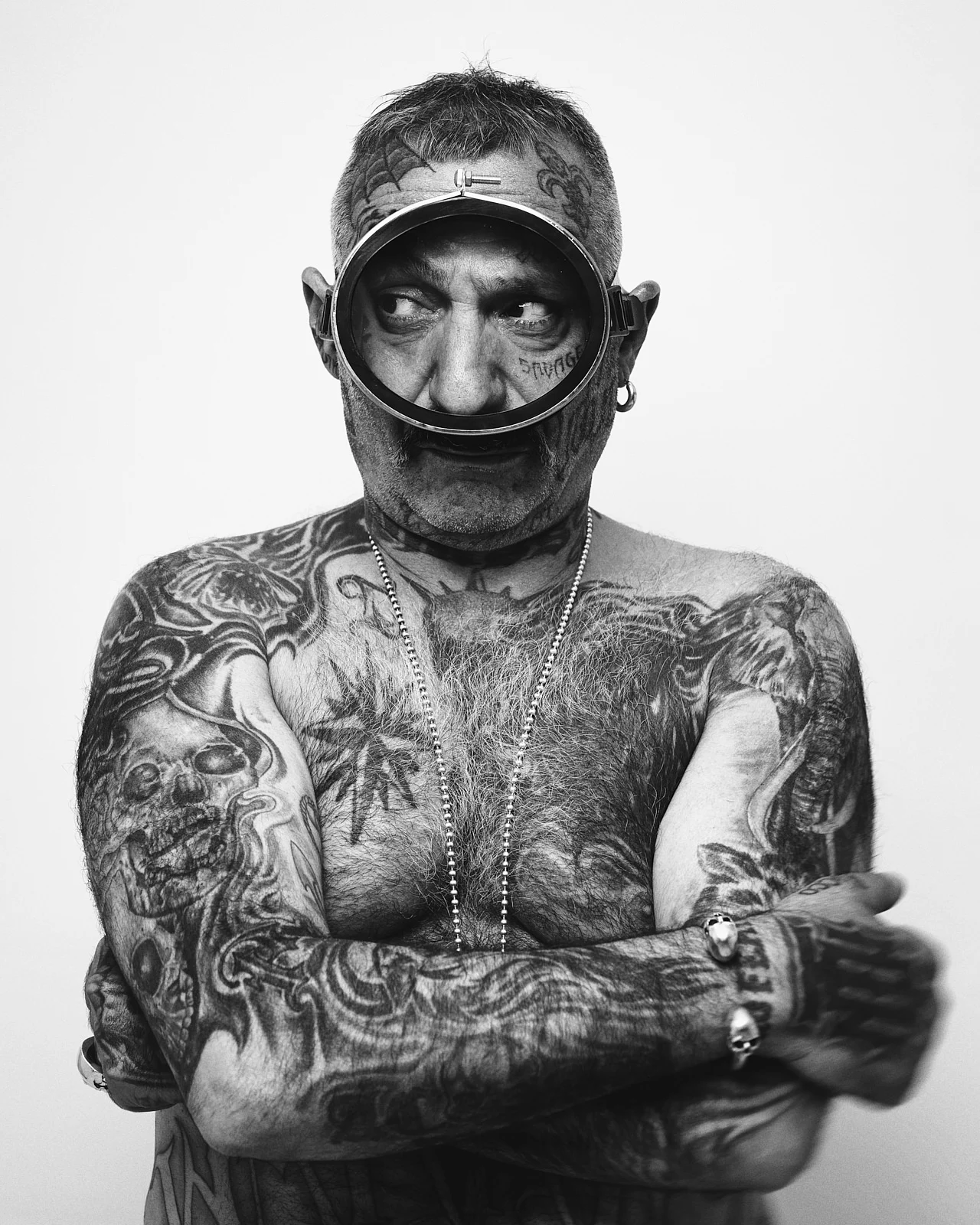 A tattooed man holding a magnifying glass in front of his eye.