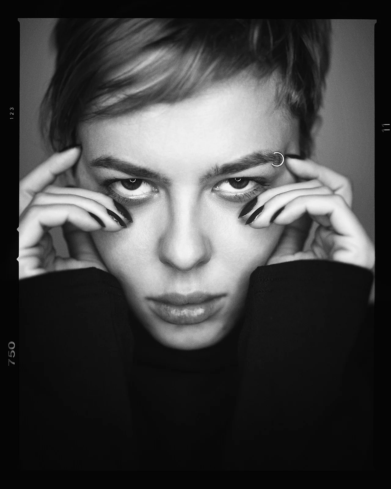 A close portrait of a short-haired woman with both hands framing her eyes.