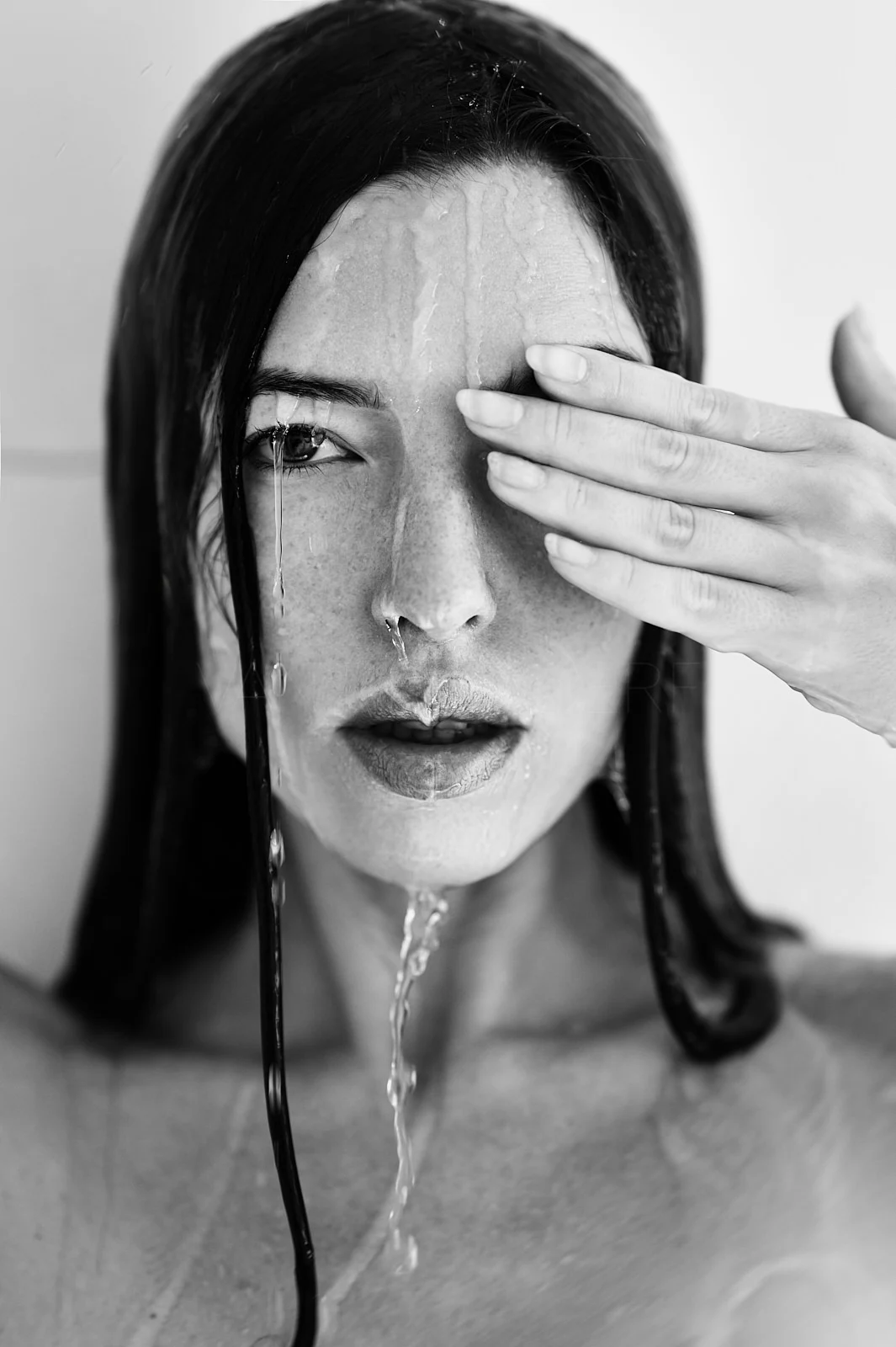 A woman with wet hair covering one eye with her hand.