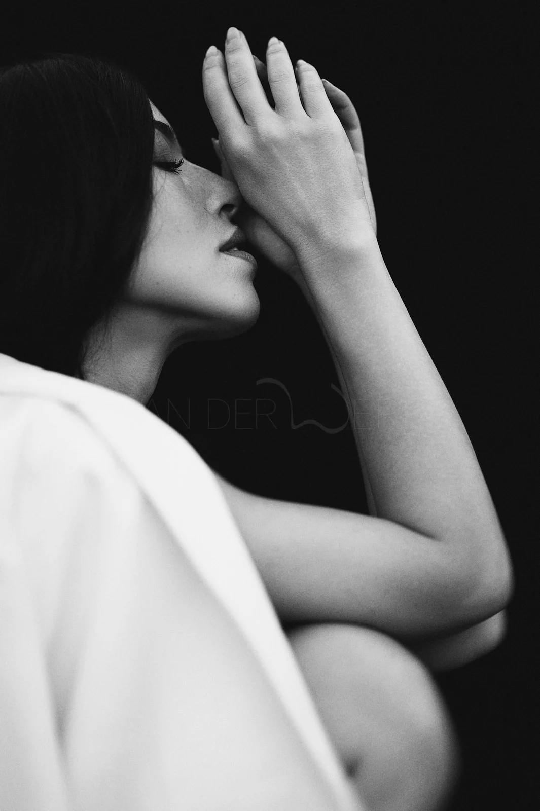 A woman's profile reflected in a dark mirror beside her raised hand.