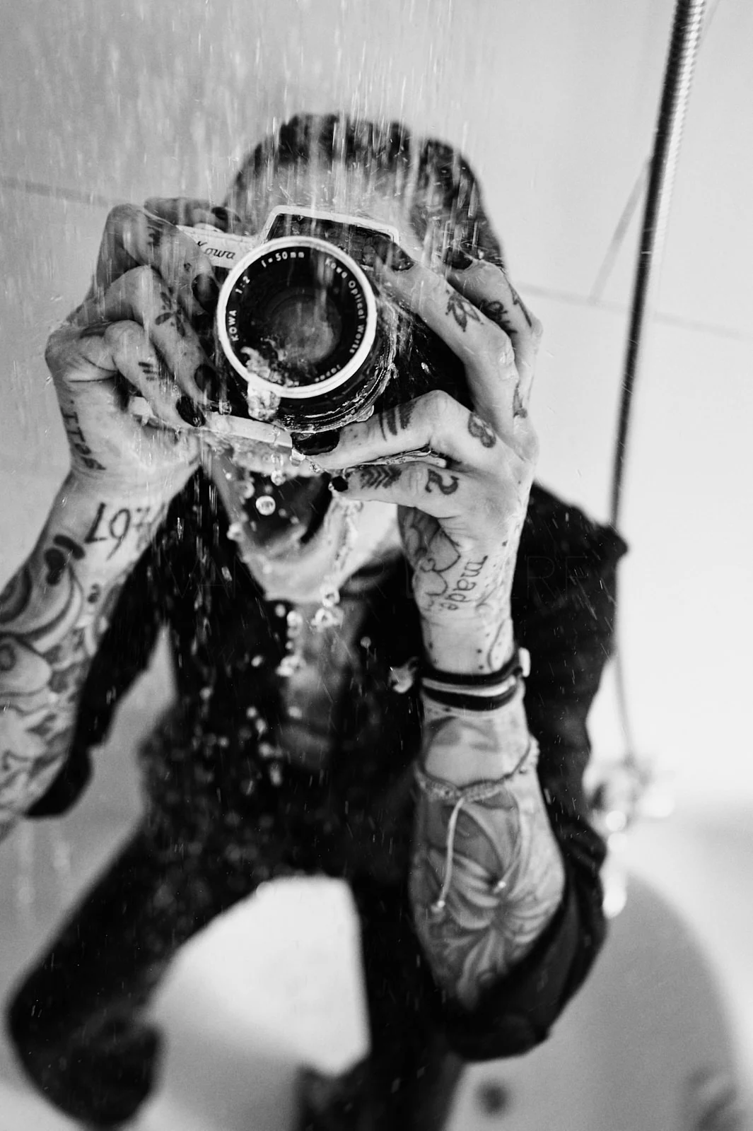 A bearded man looking through a drinking glass held in front of his eye.
