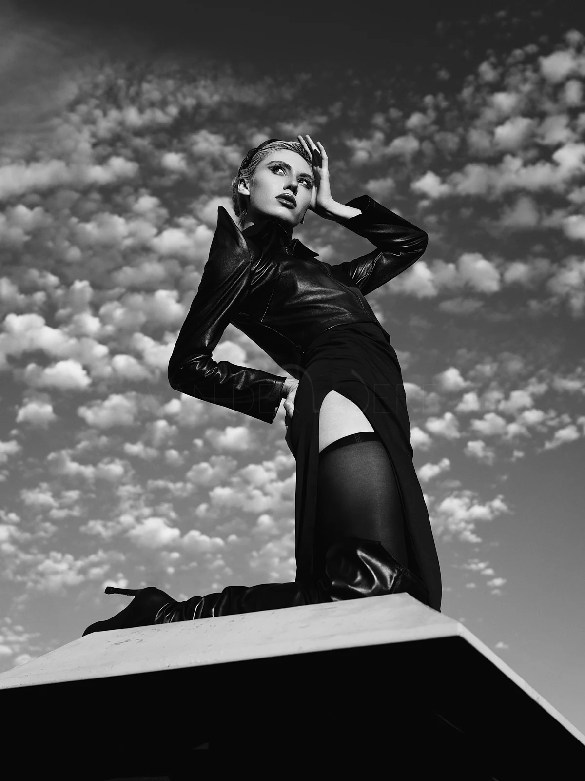 A person in a dark jacket posing on a rooftop beneath a cloud-filled sky.
