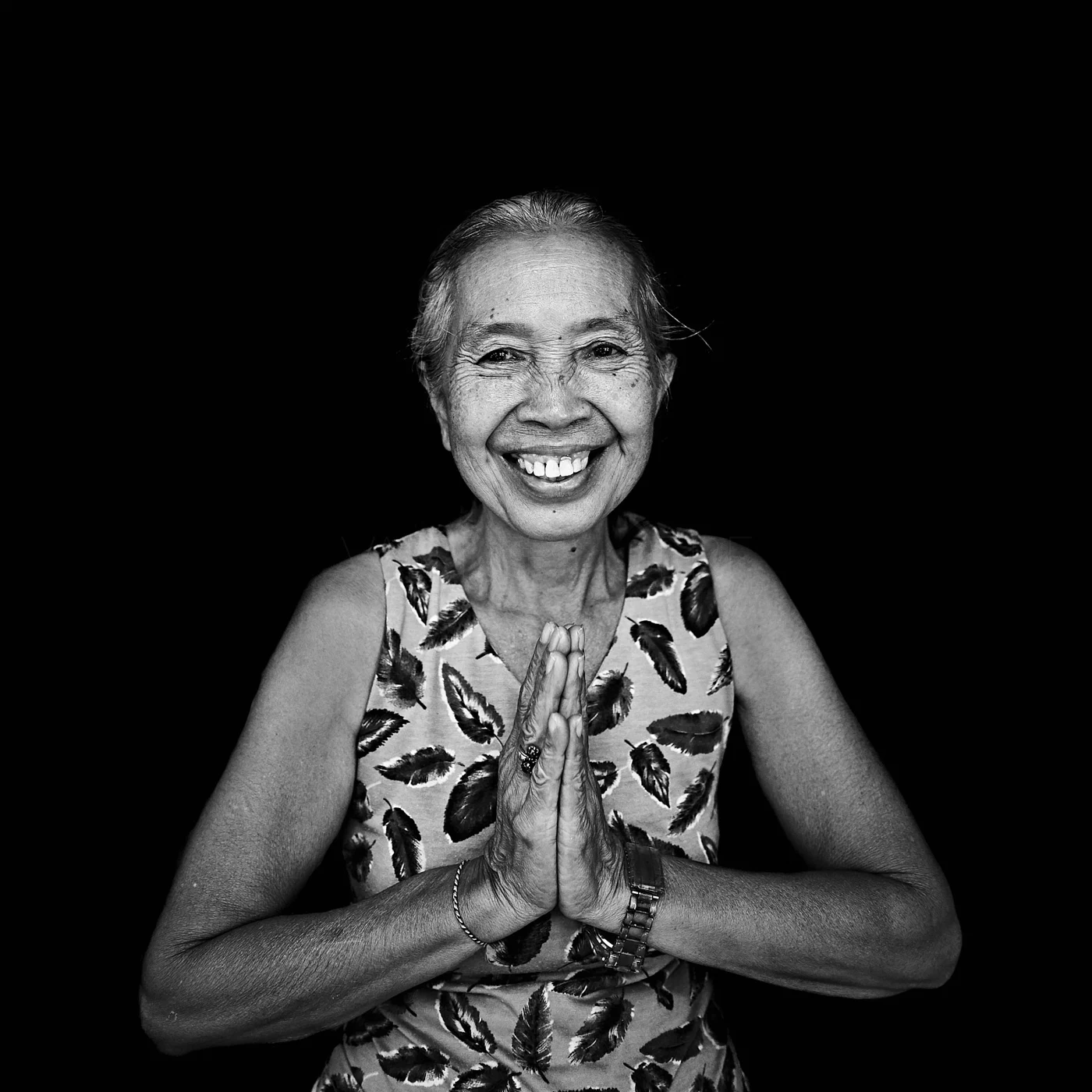 A smiling woman holding her palms together against a dark background.