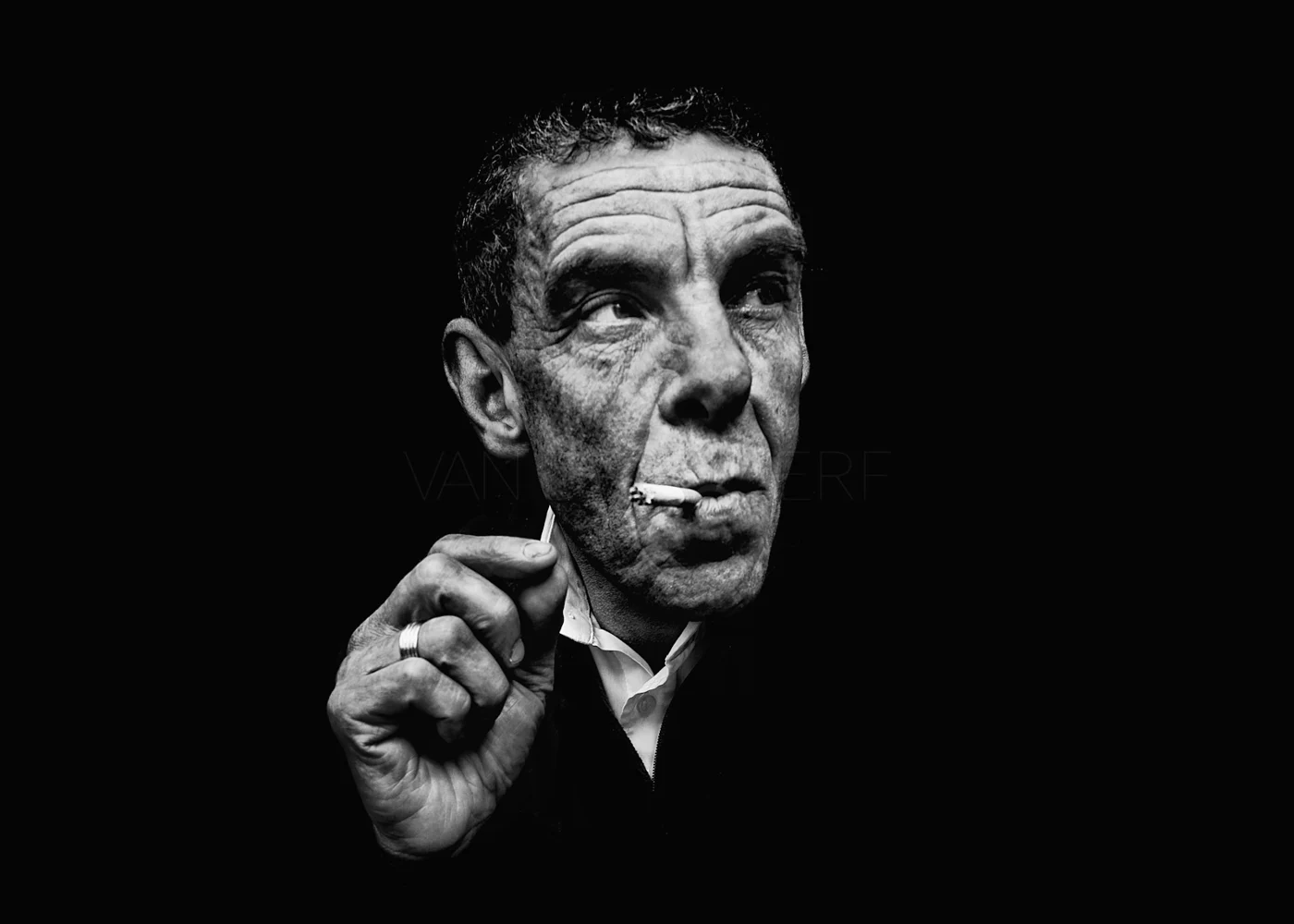 A man holding a cigarette and looking upwards in low light.