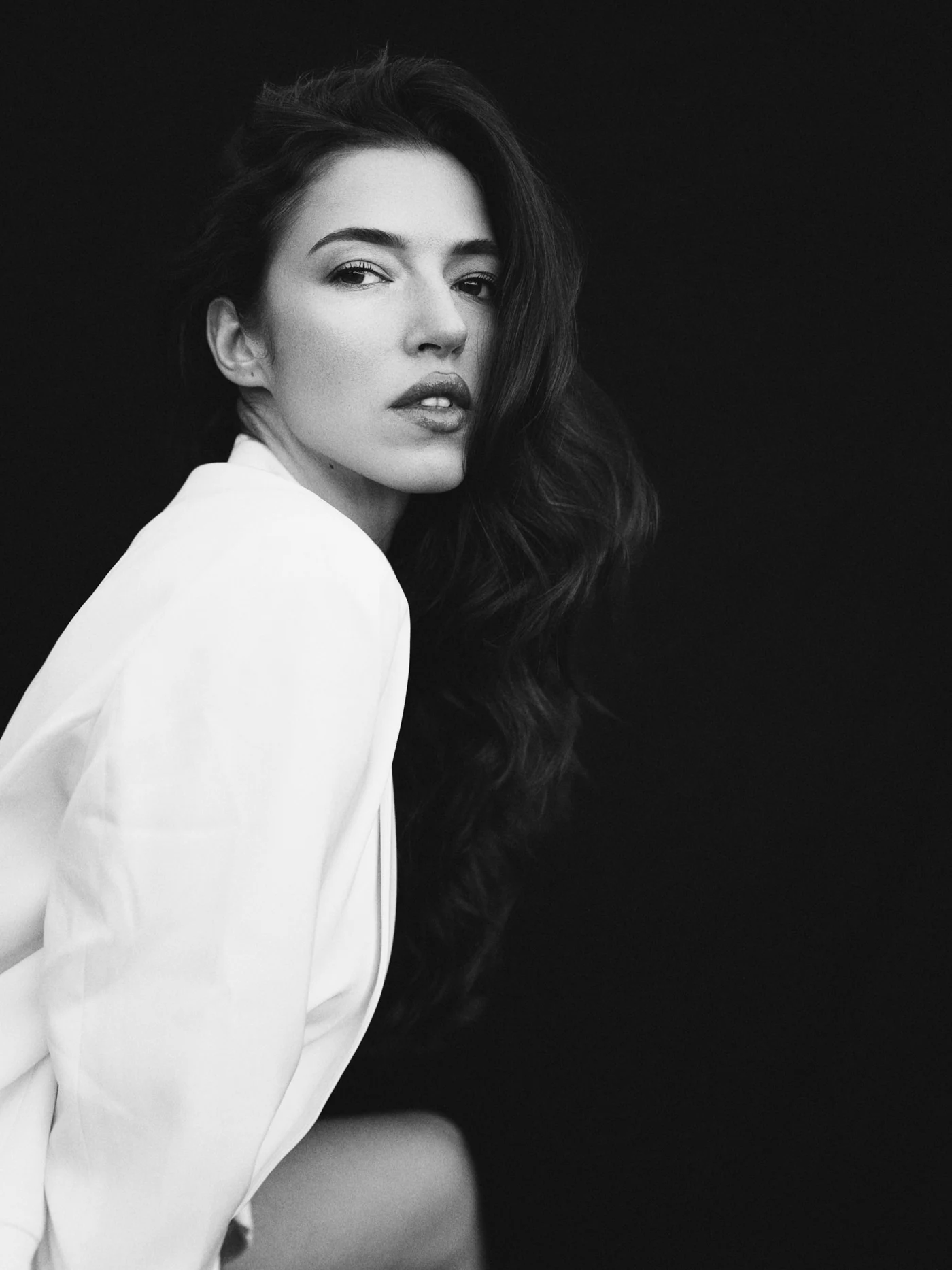 A woman in a white shirt turning towards the camera against a dark background.