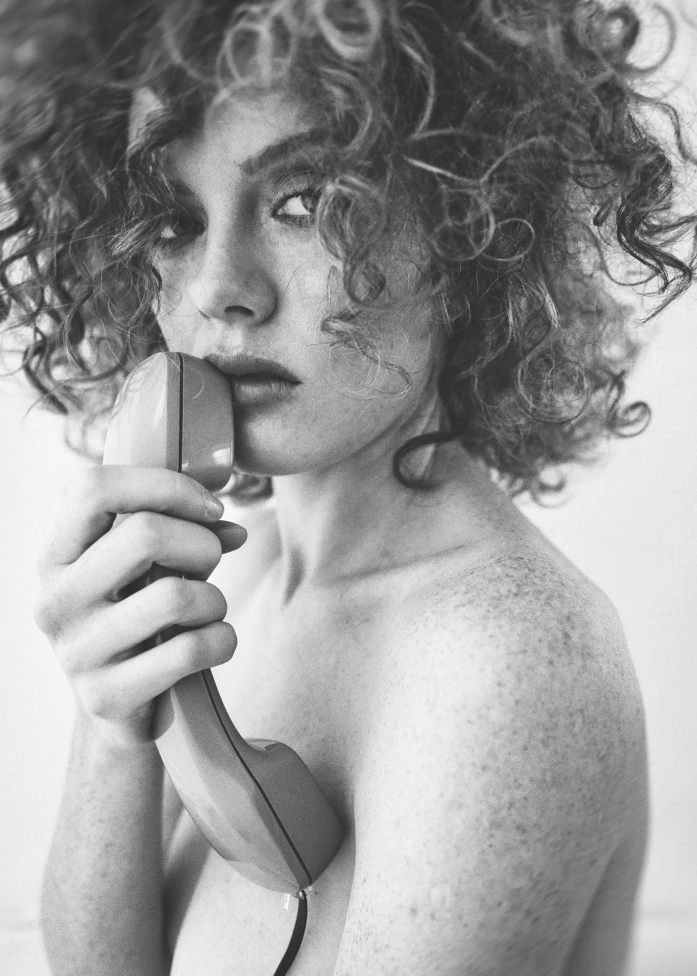 A woman with curls holding a telephone receiver close to her face.