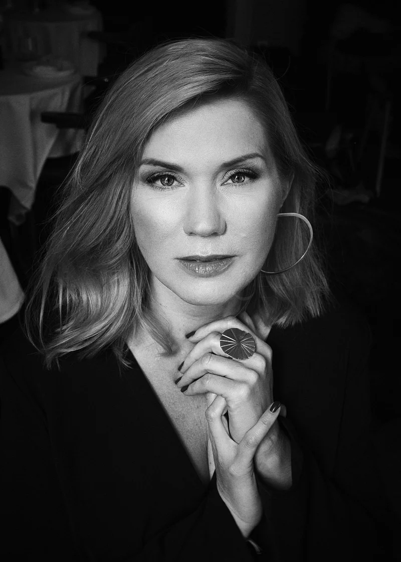Black and white portrait of a woman with shoulder-length hair wearing hoop earrings and a large ring, looking directly at the camera.