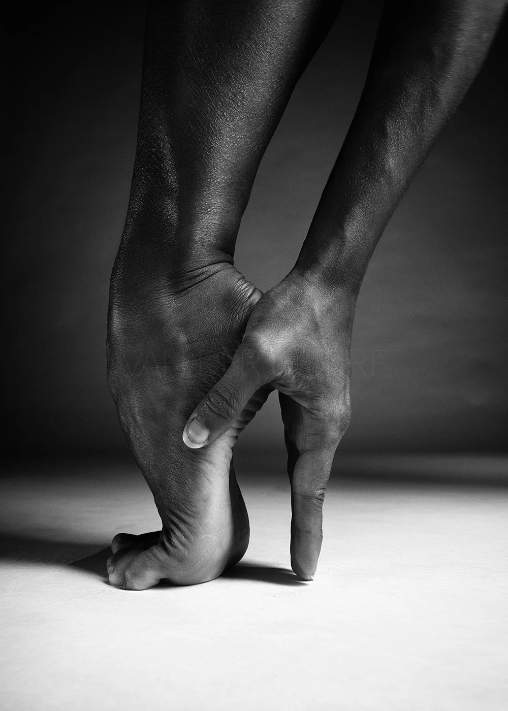 A black and white photo of a person balancing on one hand, with their fingers touching the ground and their other arm extended downward.