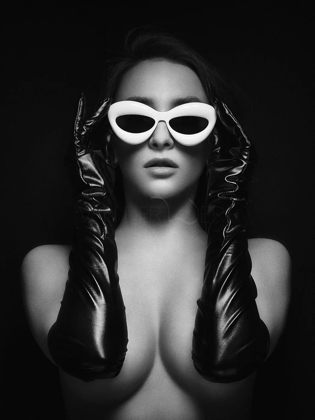 Black and white photo of a woman wearing white polarized sunglasses and long black leather gloves, posing against a dark background.