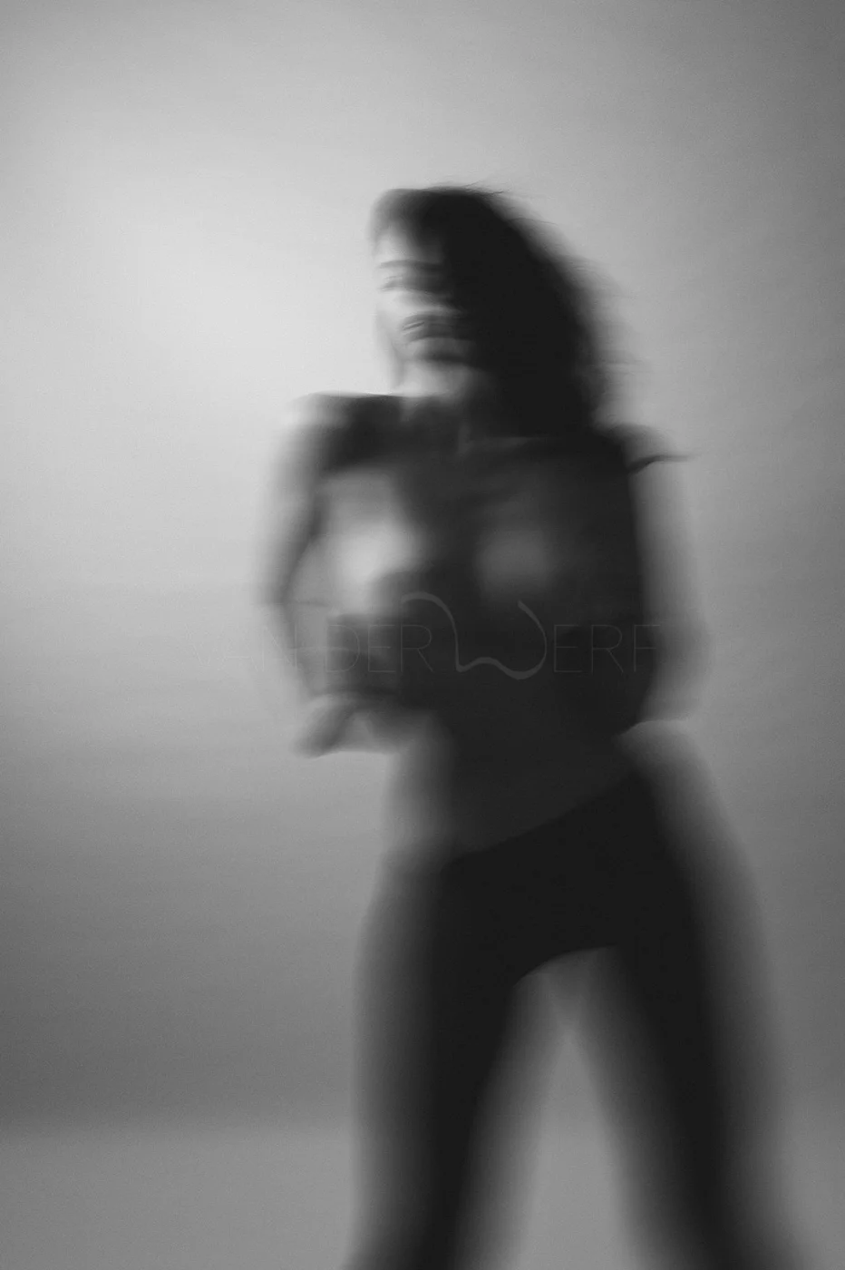 A blurry black and white photo of a woman holding a camera, standing against a plain background.
