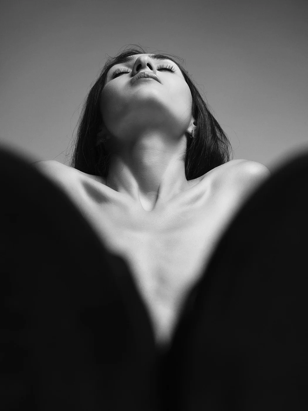 A black and white close-up photograph of a woman with her head tilted back and eyes closed, showing her neck and shoulders.