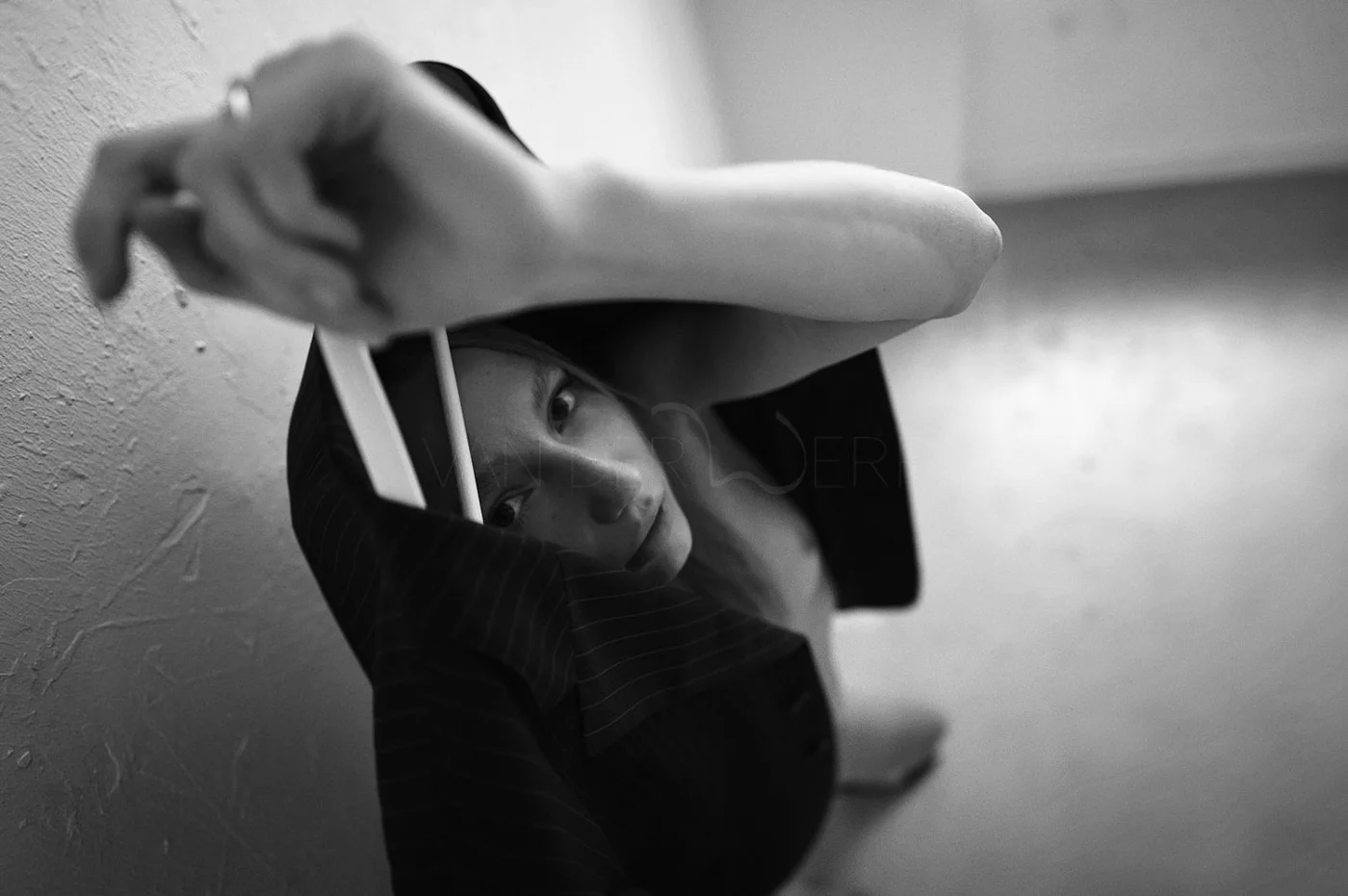 A young woman looking up at the camera from close-up, with her face partially obscured by her arm and hand, in black and white.