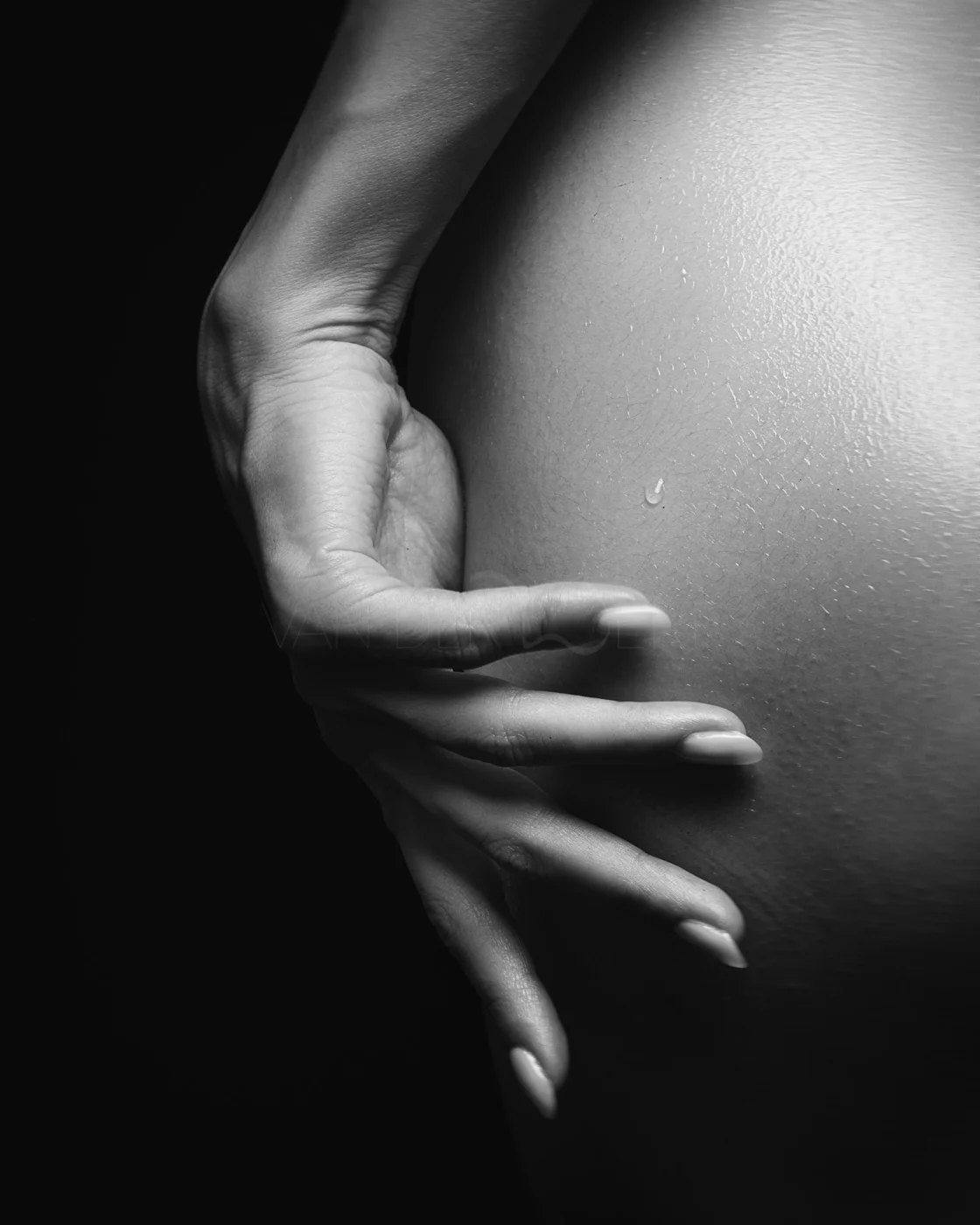 A black and white close-up of a hand gently resting on a person's back, showing textured skin and a water droplet.