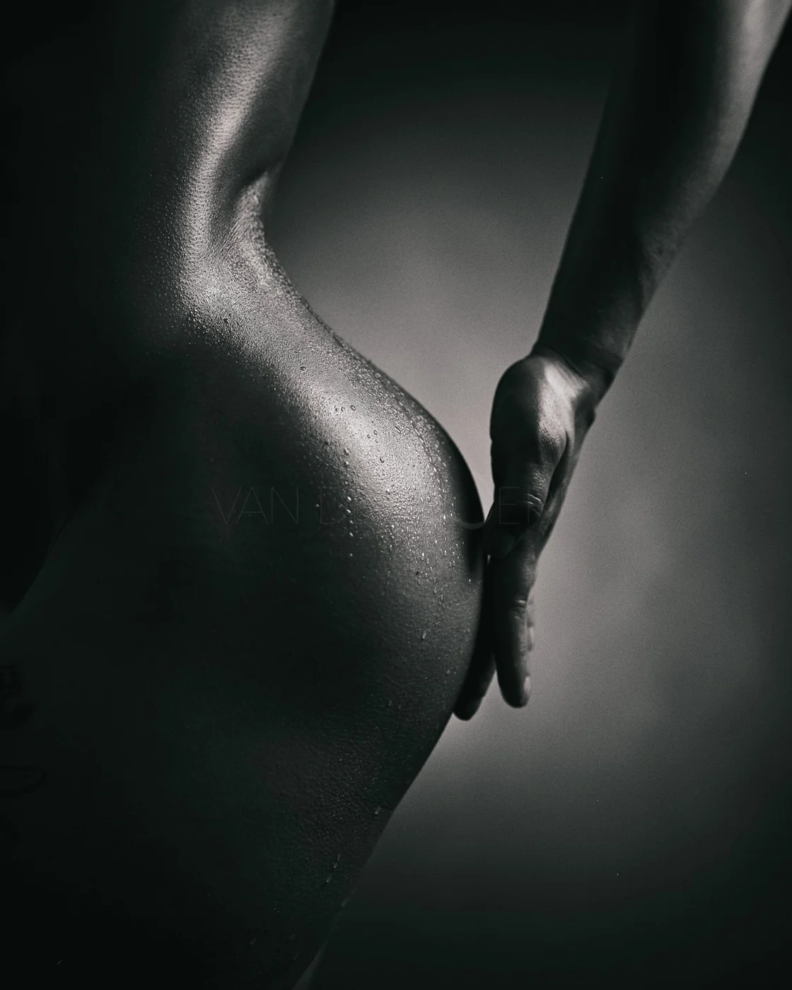 Close-up of a woman's toned back and glutes with water droplets, in black and white.