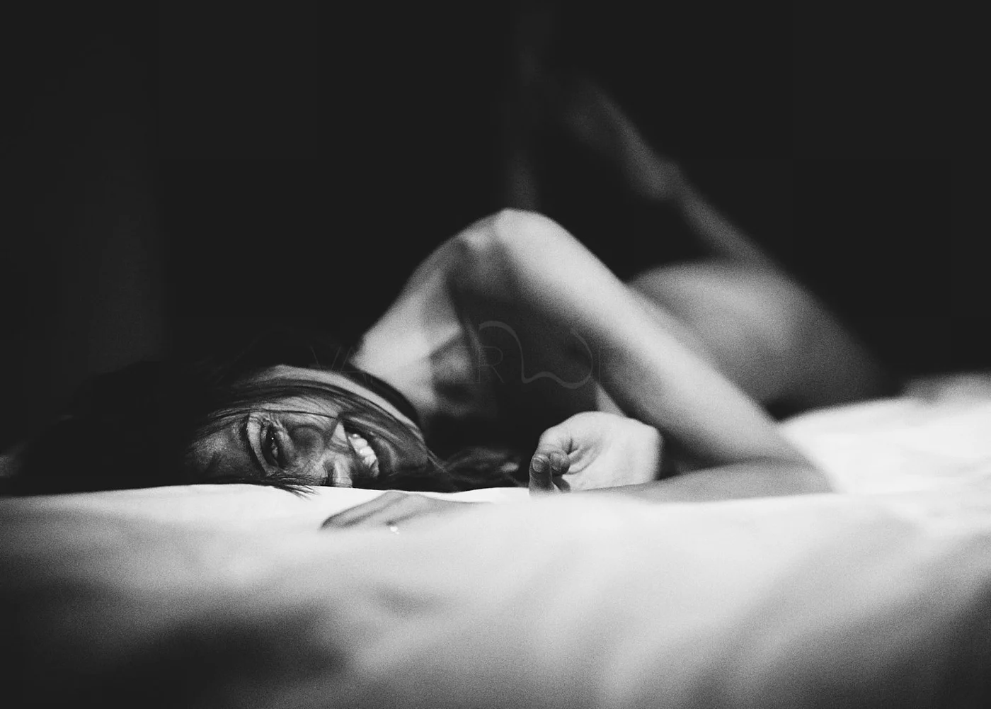 Black and white photo of a woman lying on a bed, smiling and looking at the camera.