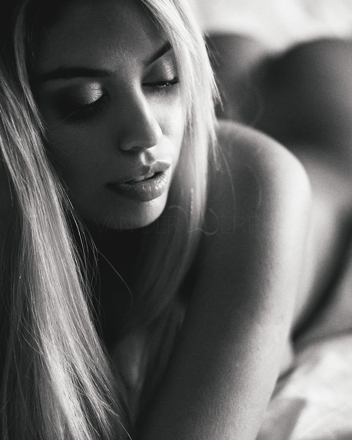 Close-up black and white portrait of a woman with long blonde hair, her eyes closed, showing her makeup and facial features.
