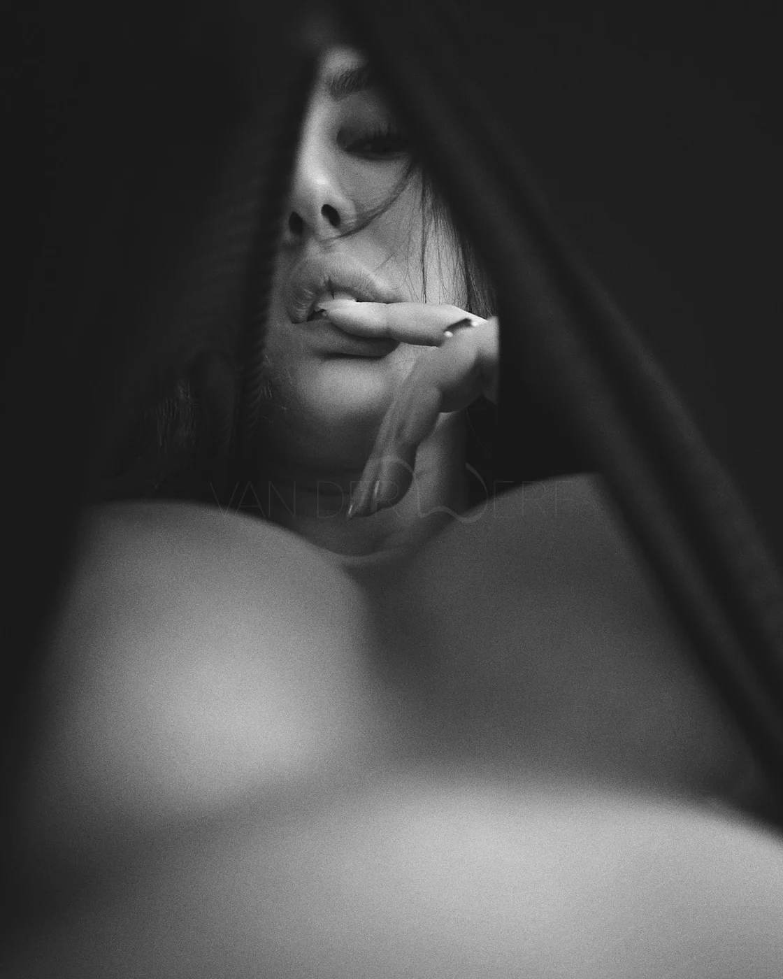 A black and white close-up of a woman’s face partially obscured by a dark fabric, with her hand near her lips, looking contemplative.
