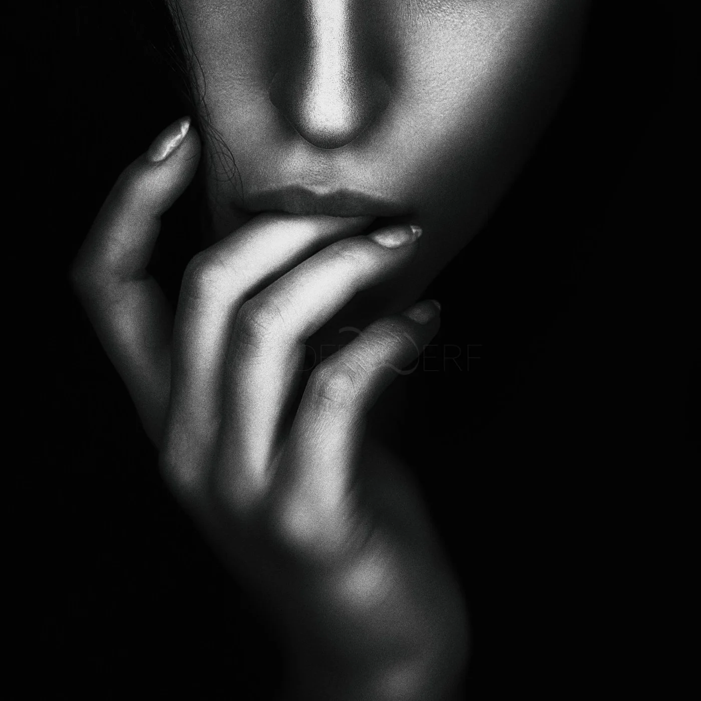 Close-up of a woman's face in black and white, with her hand near her mouth and her fingers touching her lips, creating an artistic and contemplative pose.
