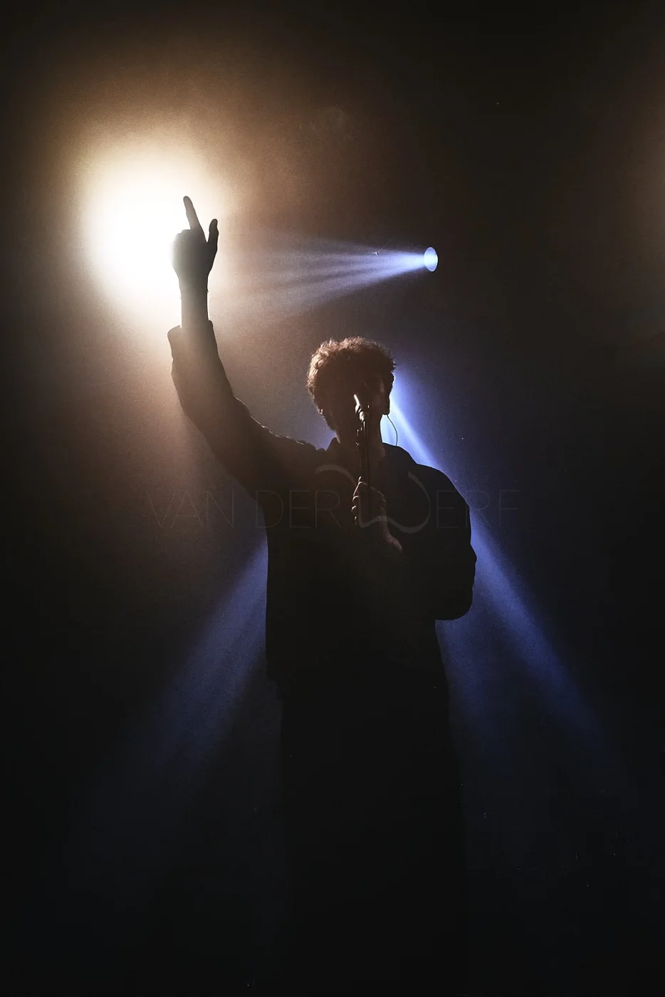 Silhouette of a person singing into a microphone on stage with lights shining behind, creating a dramatic effect.