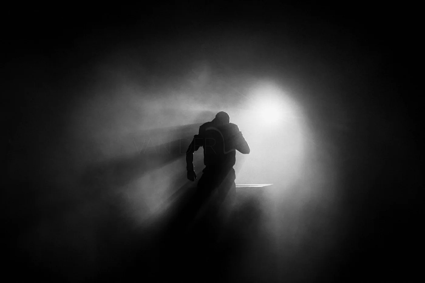 Silhouette of a person running towards a bright light in a dark environment.
