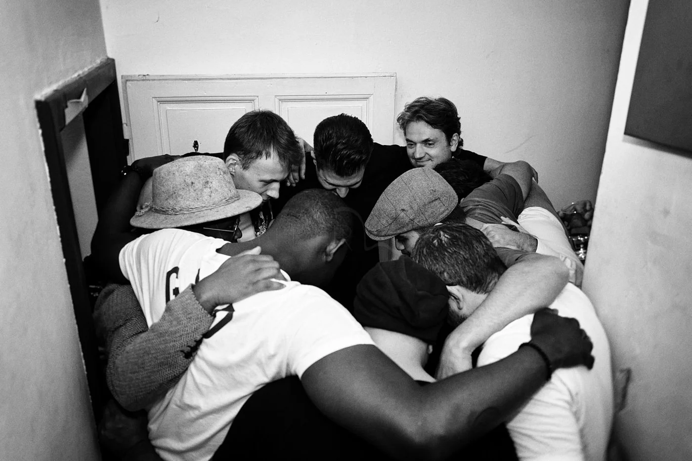 A group of men huddled together in a close embrace in a small room with plain walls.